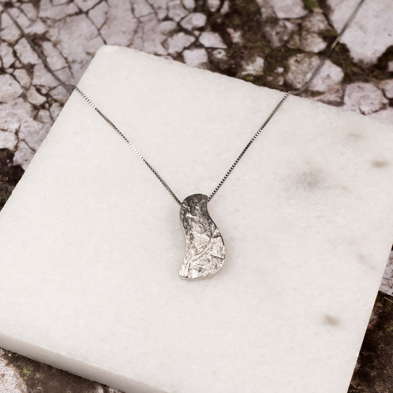 Contemporary sterling silver pendant with an organic, asymmetrical shape and hammered texture, suspended on a delicate box chain for a modern, sculptural look.