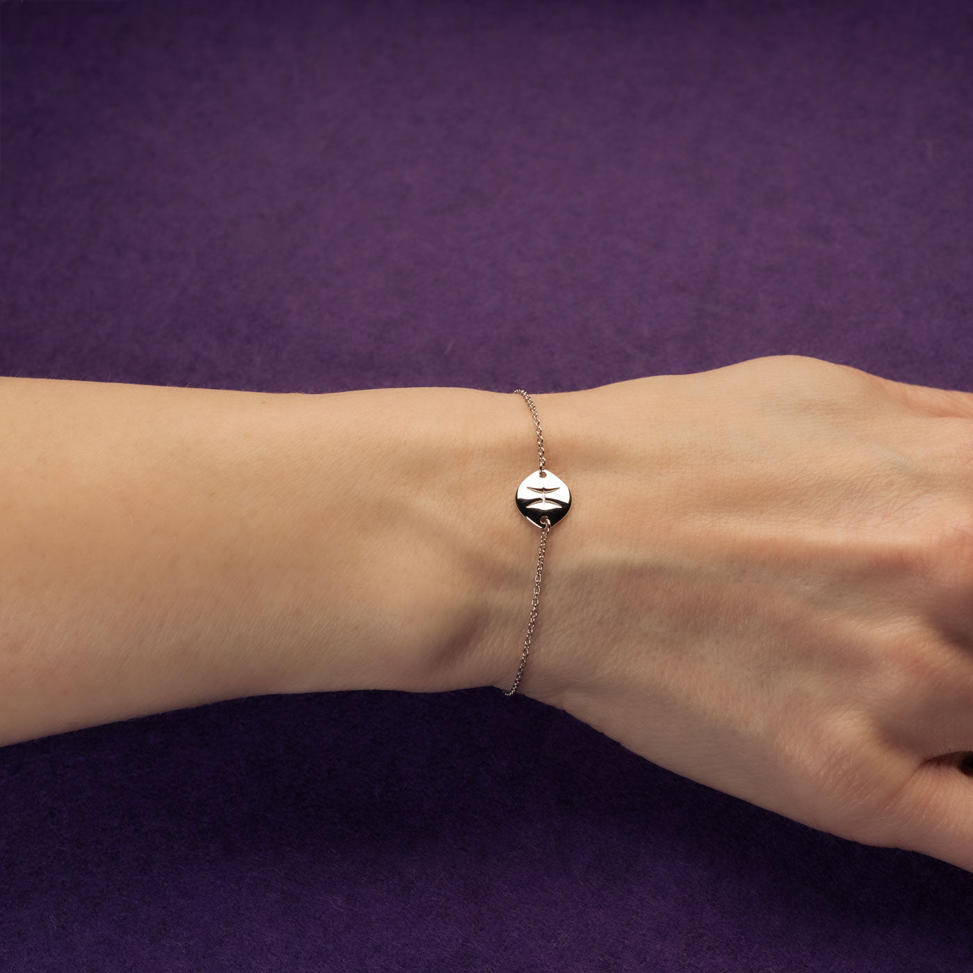 Delicate sterling silver adjustable bracelet featuring a polished Pisces zodiac charm on a fine chain, styled on a wrist against a rich purple background.