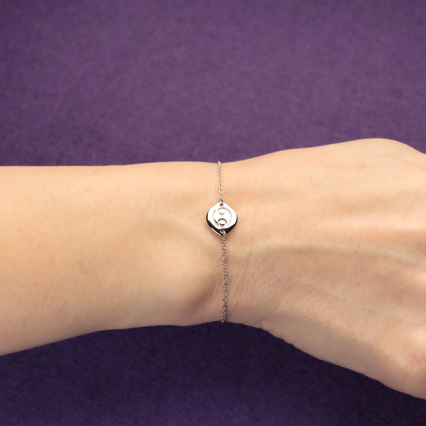 Delicate sterling silver bracelet featuring an adjustable sliding bead and a sculptural Cancer zodiac charm, styled on a wrist against a deep purple background.