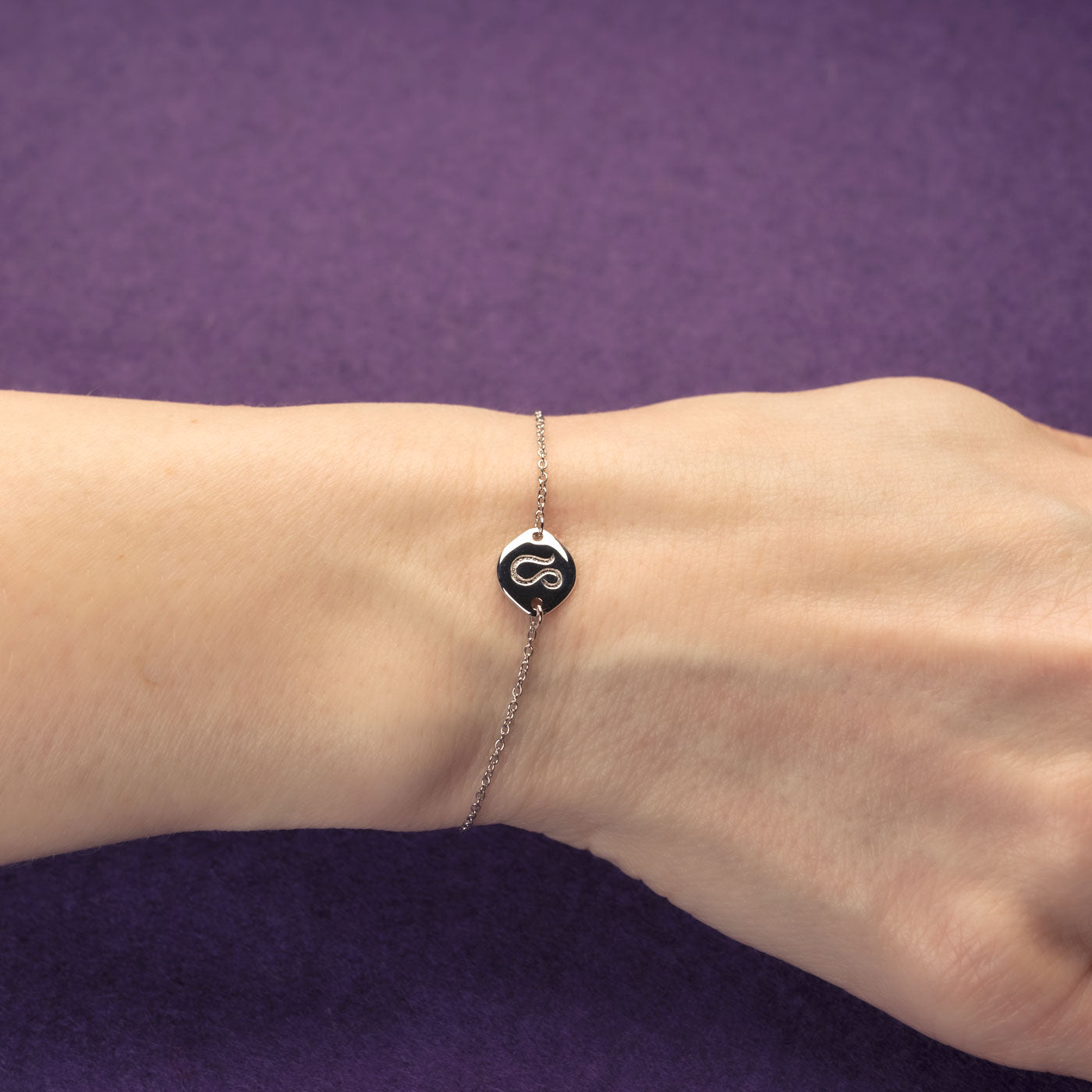 Delicate sterling silver bracelet featuring an adjustable chain with a polished Leo zodiac charm, worn on the wrist against a purple background.