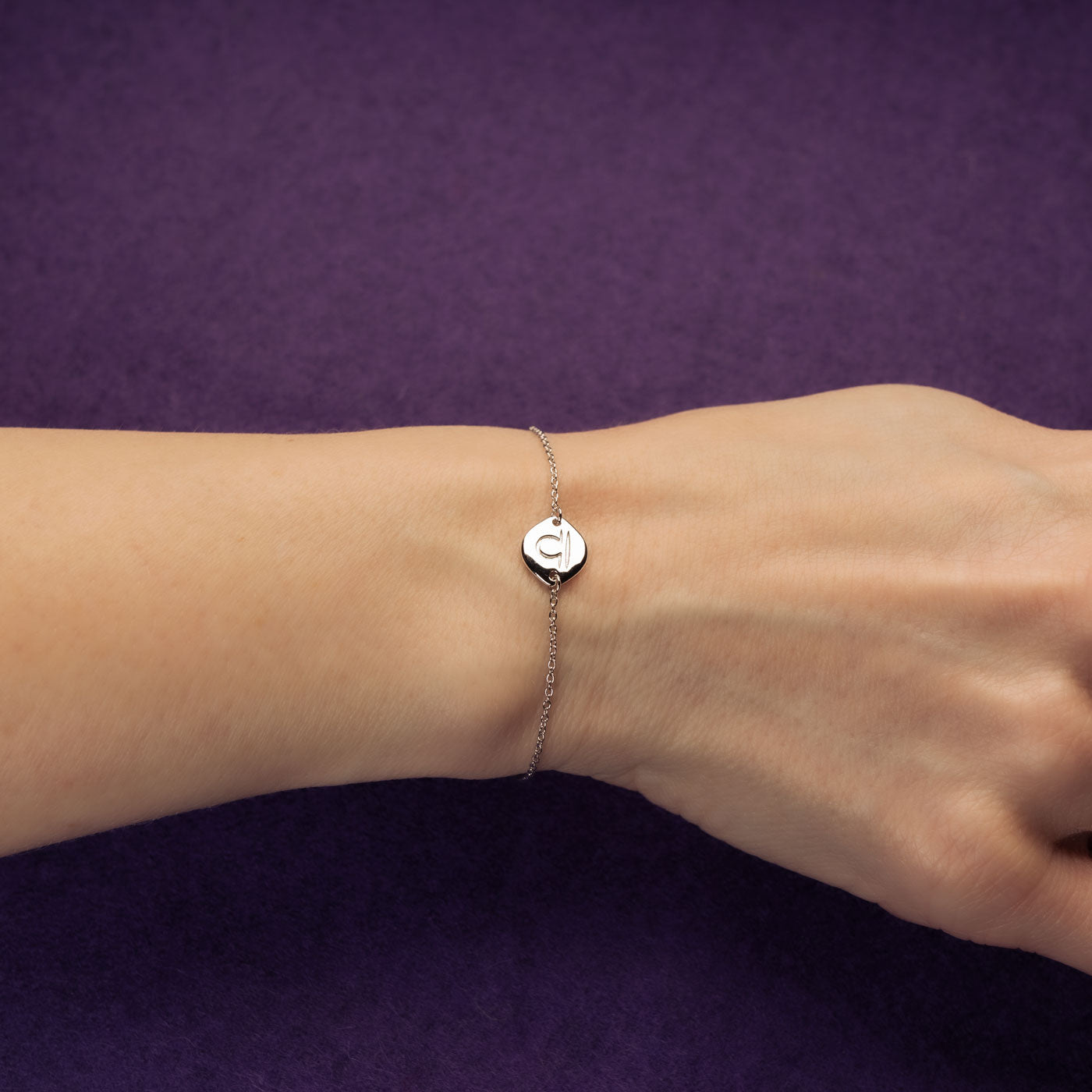Delicate sterling silver bracelet featuring a small Libra zodiac charm on a fine adjustable chain, worn on the wrist against a rich purple background.