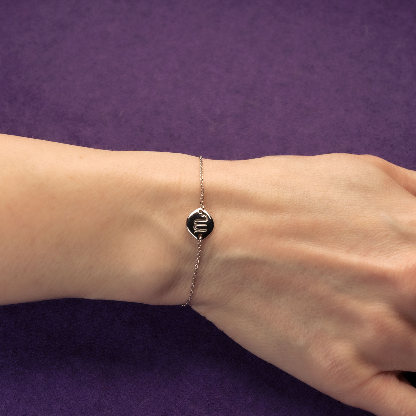 Delicate sterling silver adjustable bracelet featuring a polished Scorpio zodiac symbol charm on a fine chain, displayed on a wrist against a purple background.