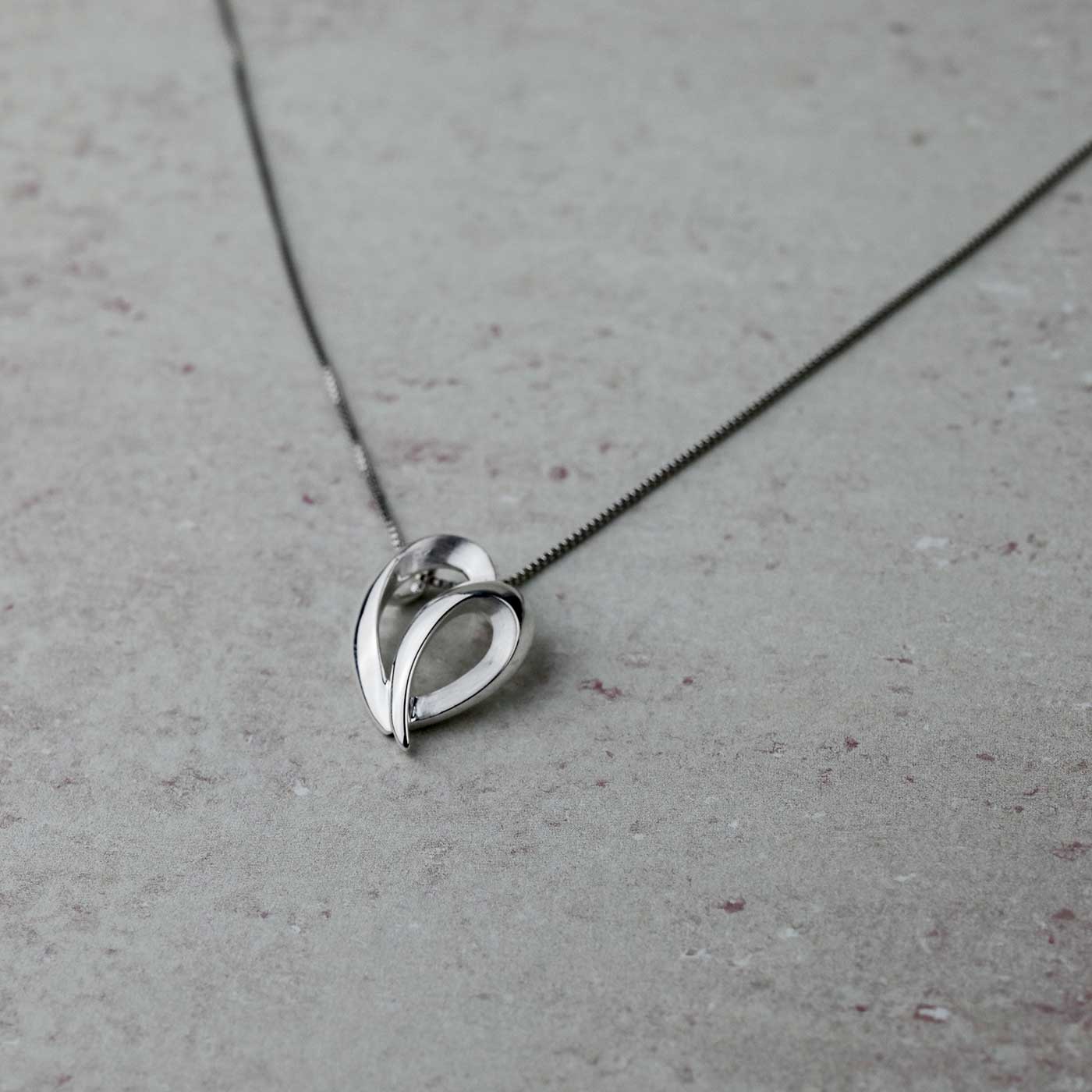 Polished sterling silver pendant with a sculptural, curved heart design suspended from a delicate chain, exemplifying refined contemporary silver jewellery by Azendi.