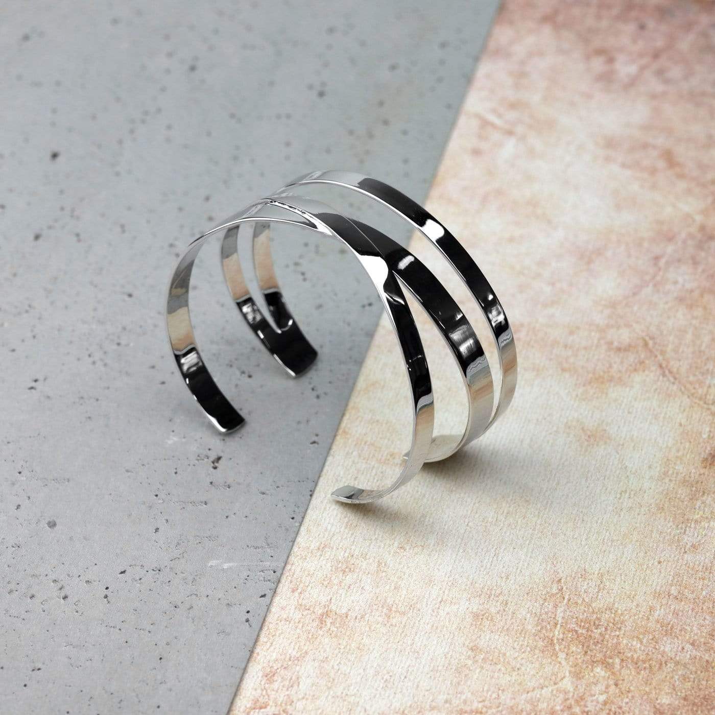 Polished sterling silver cuff bangle featuring three intertwined strands with a contemporary crossover design, reflecting refined British silver jewellery artistry.