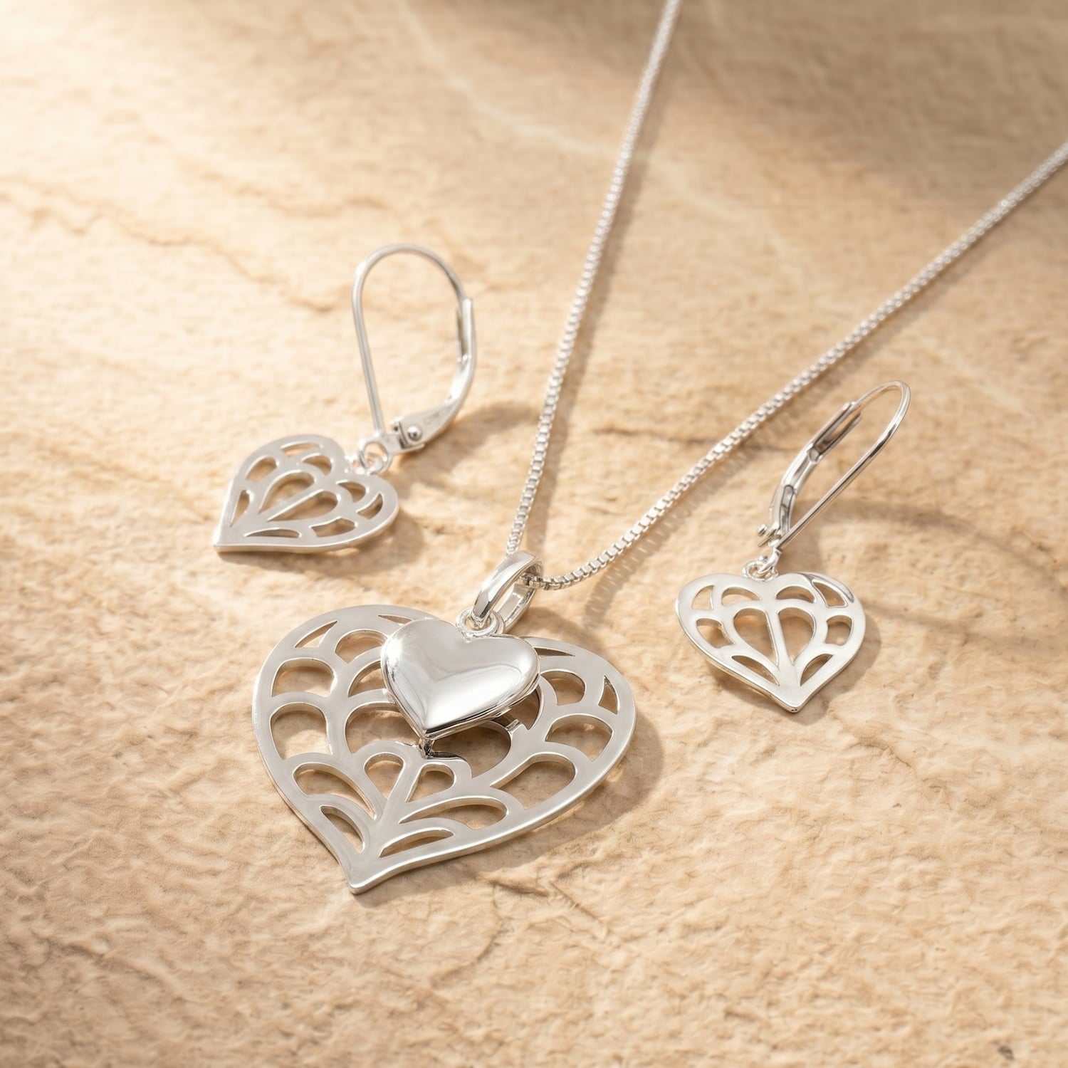 Sterling silver jewellery set featuring an intricate double heart pendant with a smooth heart overlay and matching earrings, showcasing sculptural Yorkshire-inspired design.