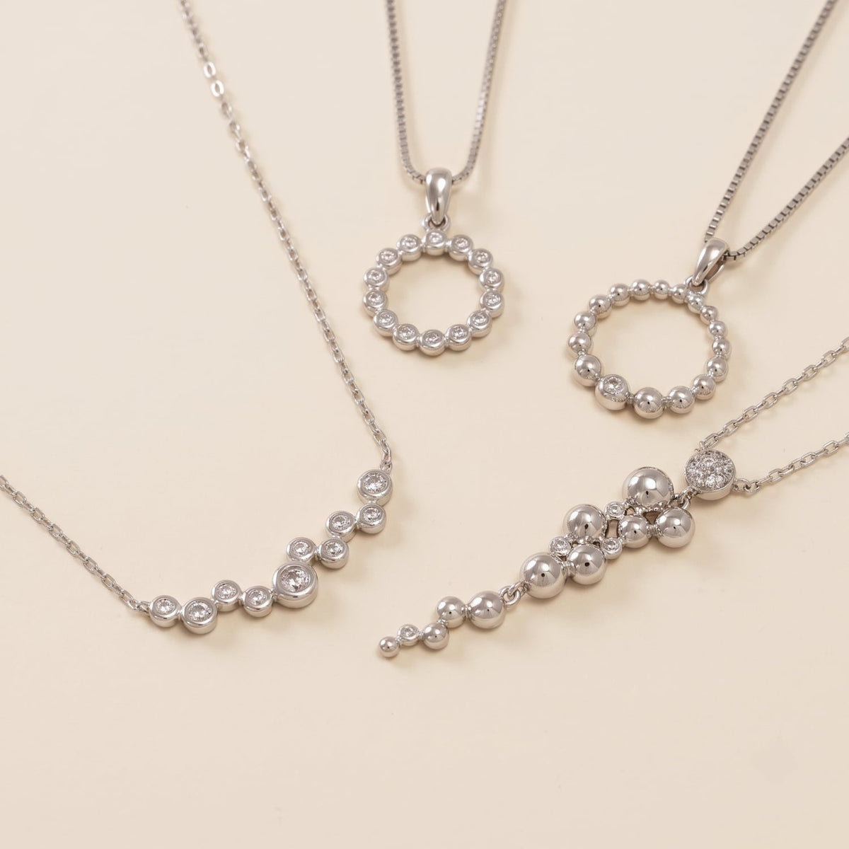 Collection of contemporary sterling silver necklaces featuring various sculptural bead and cubic zirconia designs on delicate chains displayed on a cream surface.