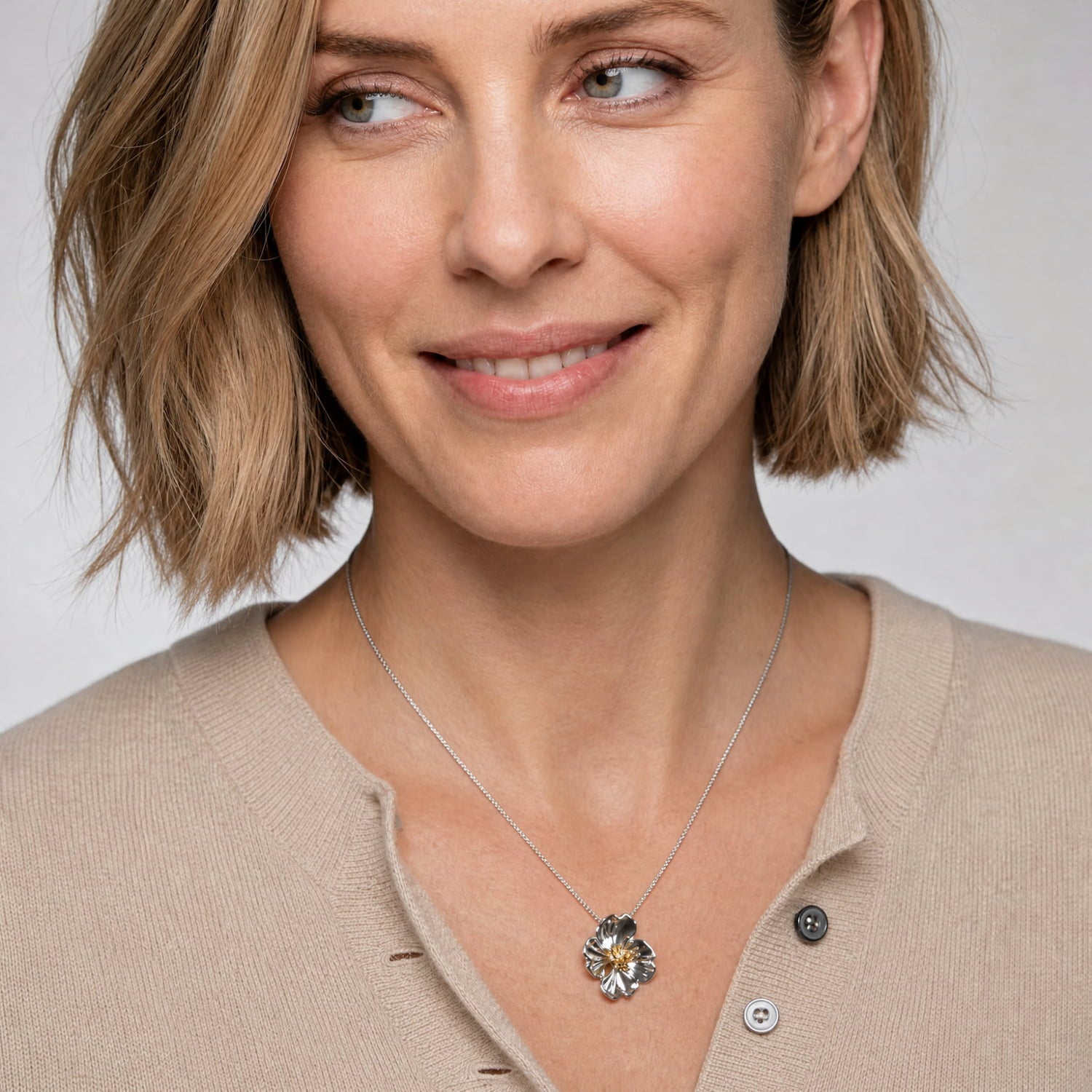 Sterling silver pendant shaped as a detailed primrose flower with a warm golden center, suspended from a fine chain, styled against a camel cashmere cardigan.