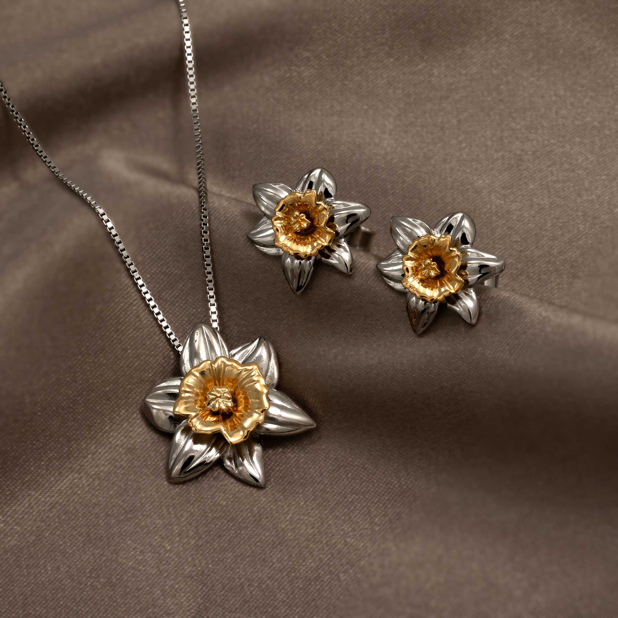 Sterling silver and gold vermeil floral pendant and matching earrings inspired by daffodil blooms, displayed on a smooth taupe satin background.
