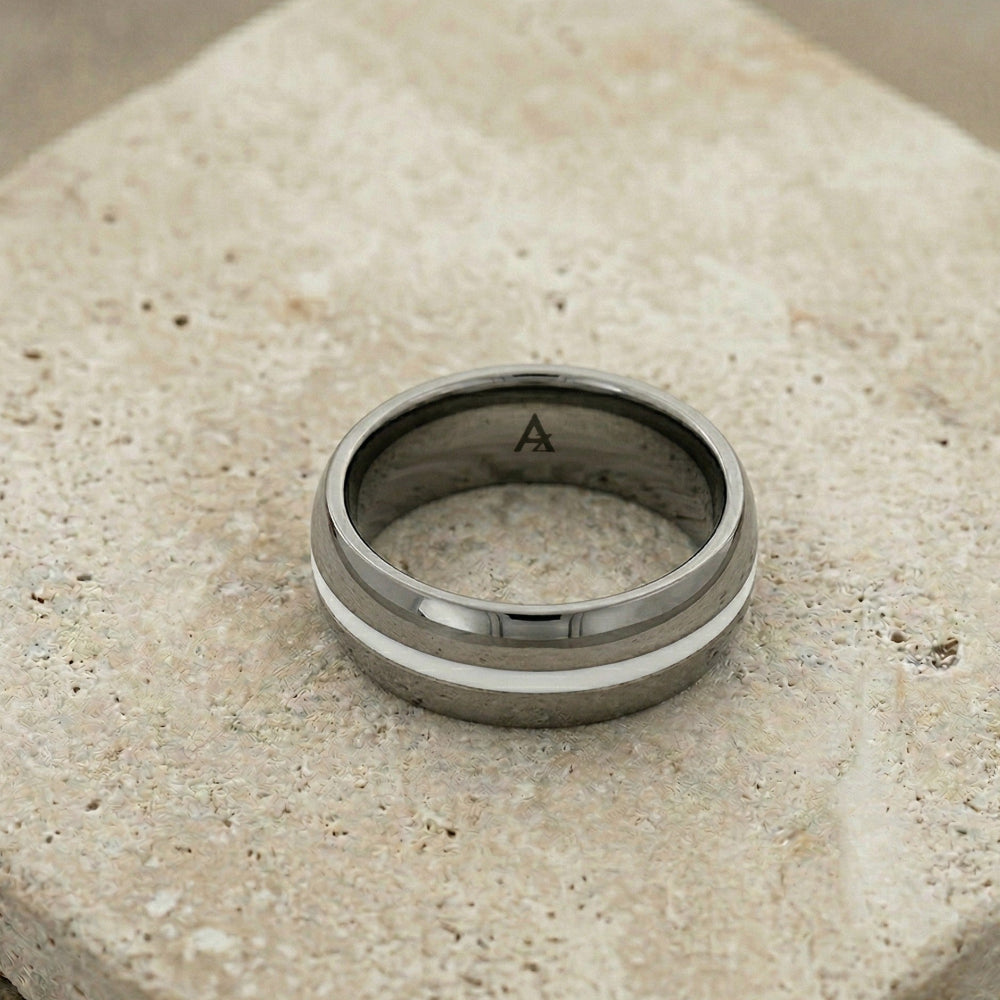 Wide tungsten ring featuring a polished silver stripe encircling the band, showcasing a sleek and modern design on a textured neutral stone surface.