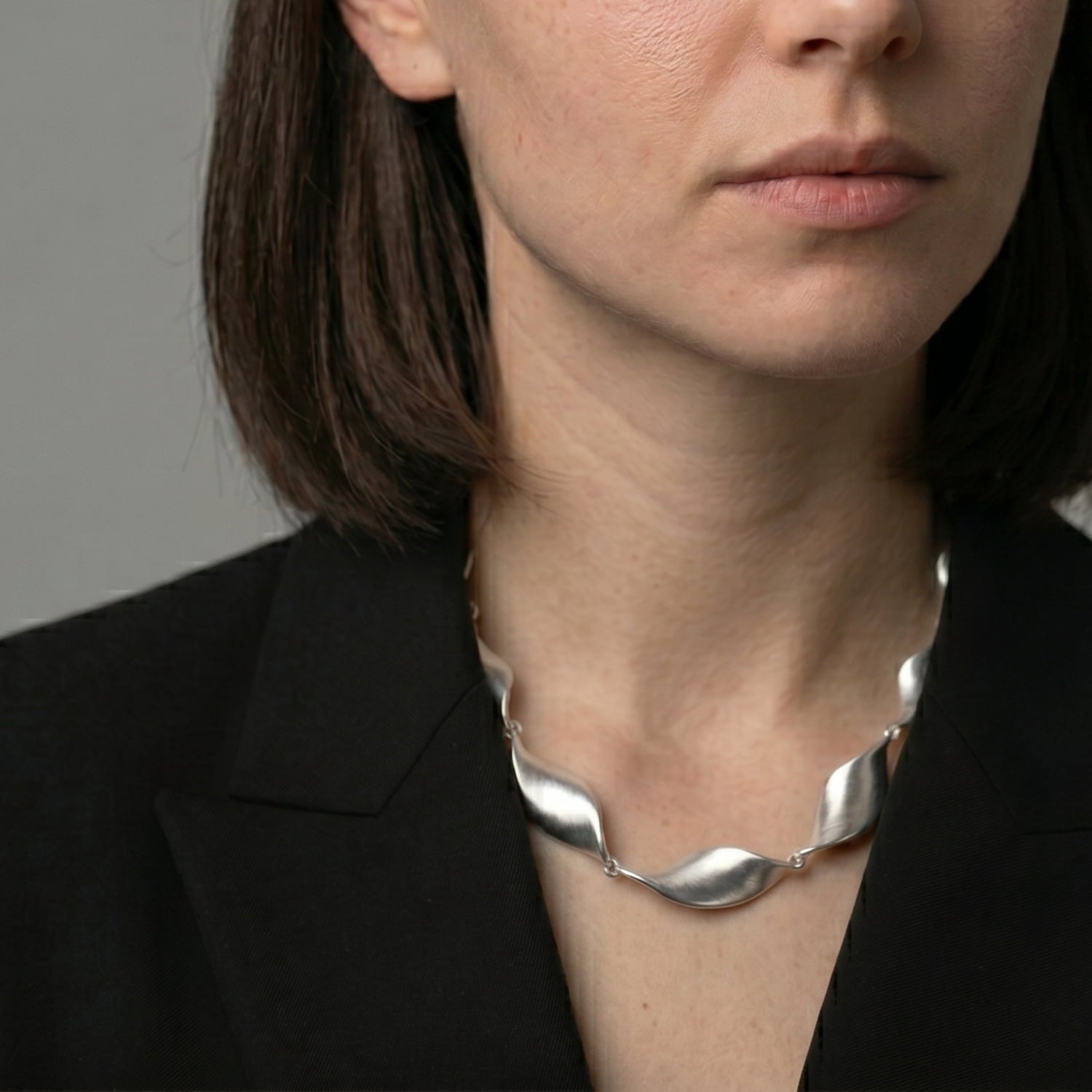 Woman wearing a silver twisting necklace against a neutral background