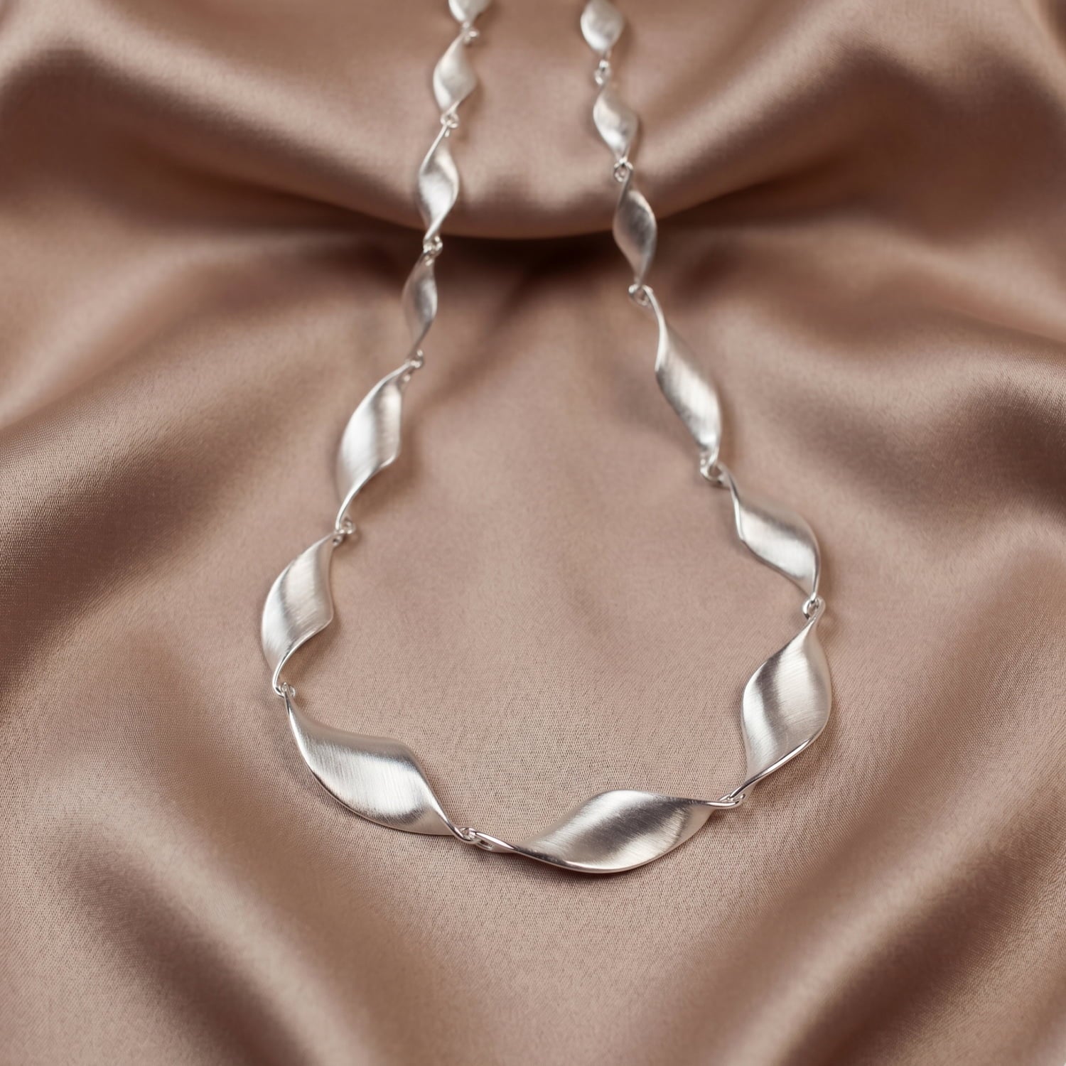 Silver twisting link necklace on a beige fabric background