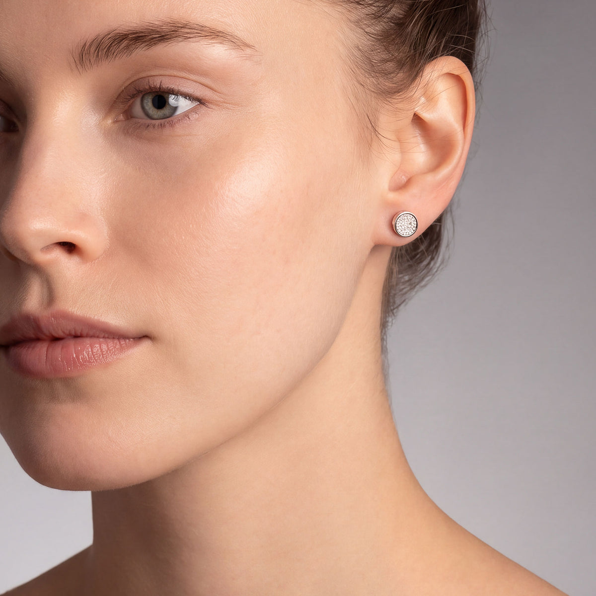 A close-up of a woman's ear wearing a small round stud earring with cubic zirconia centre.