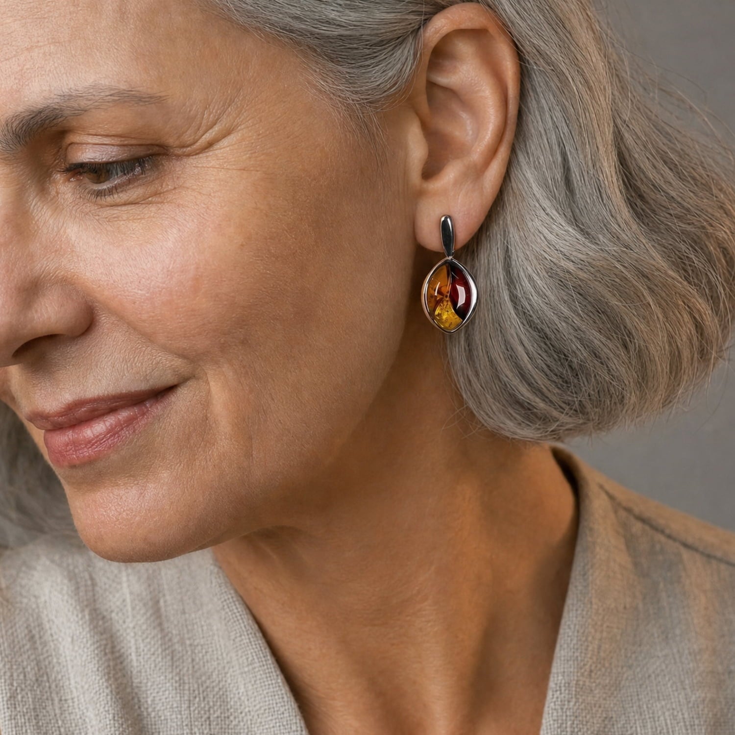 A close-up of a woman with grey hair wearing a teardrop-shaped three-colour amber drop earring.
