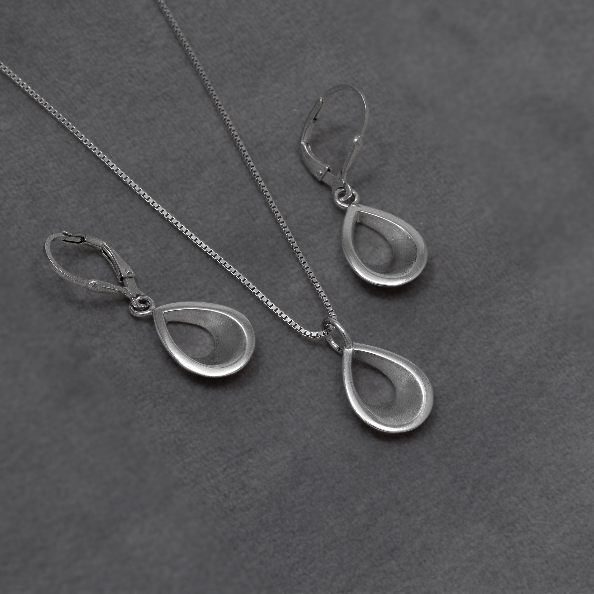 Silver teardrop drop earrings and matching pendant necklace on a textured grey background.