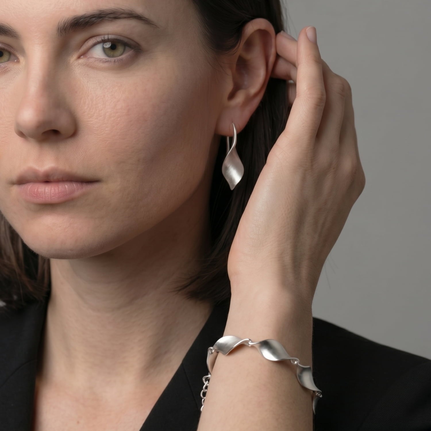 Woman wearing silver earrings and bracelet against a neutral background