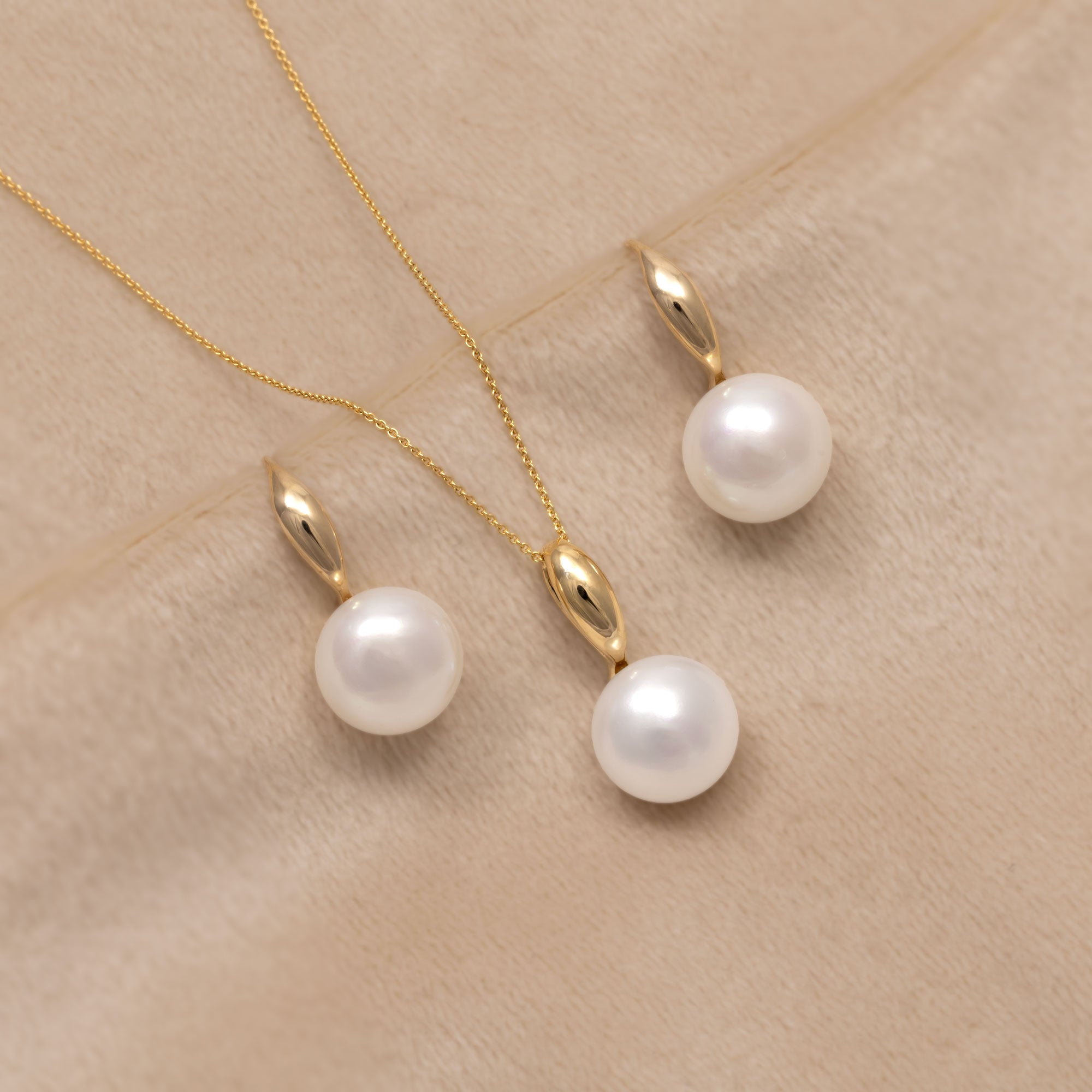 A delicate 9ct gold necklace and matching drop earrings with a single white pearl pendant. Placed on a cream velvet cloth.