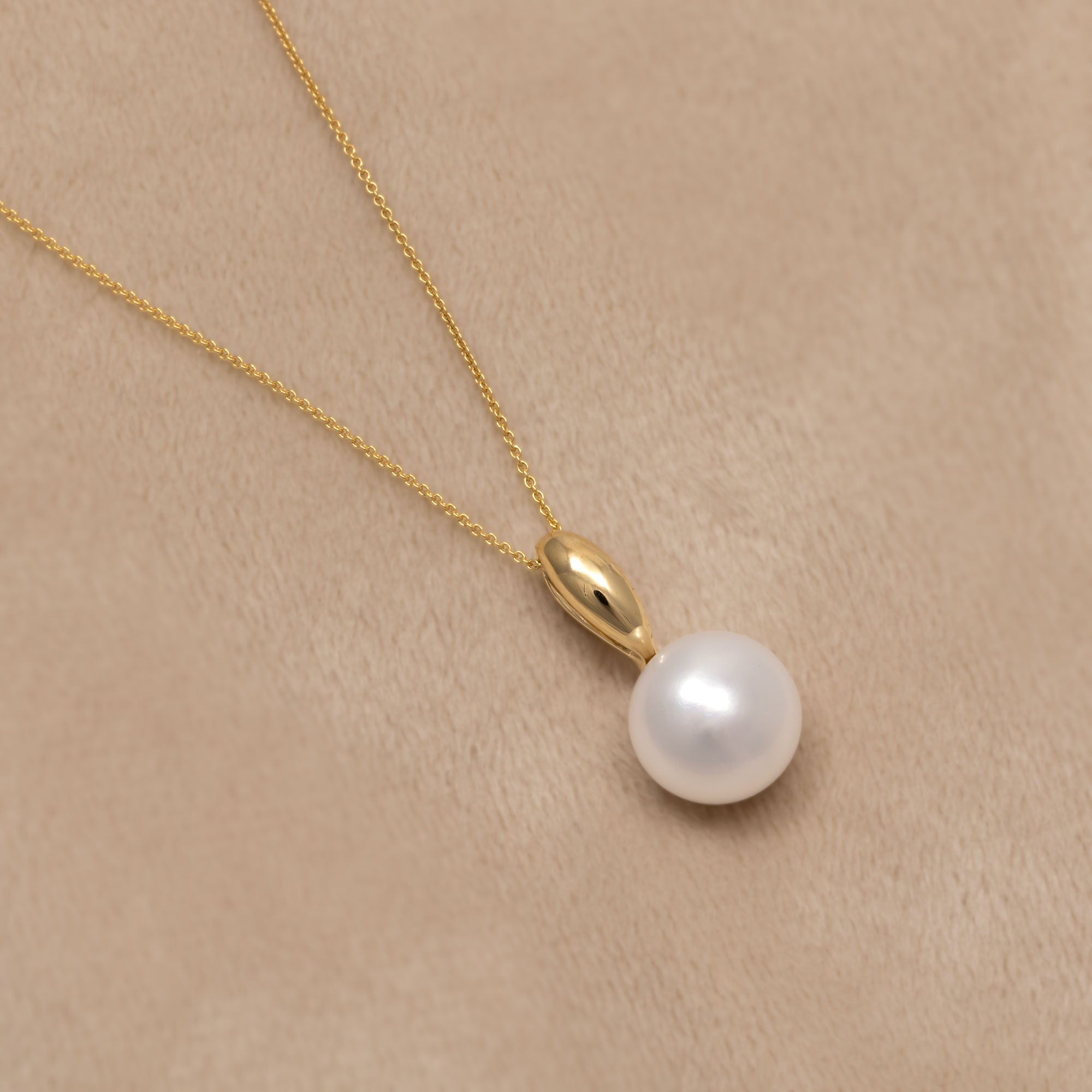 A delicate 9ct gold necklace with a single white pearl pendant. Placed on a cream velvet cloth.
