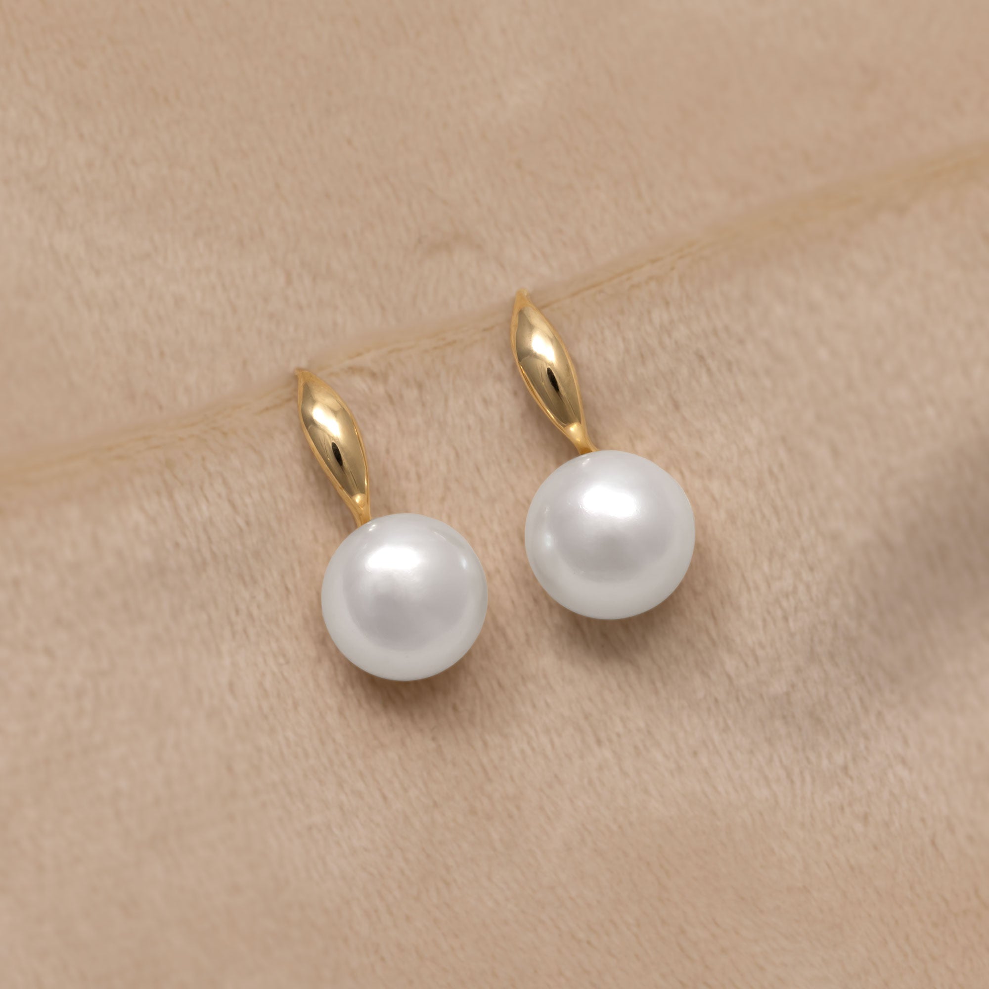 Delicate 9ct gold drop earrings with a single white pearl. Placed on a cream velvet cloth.