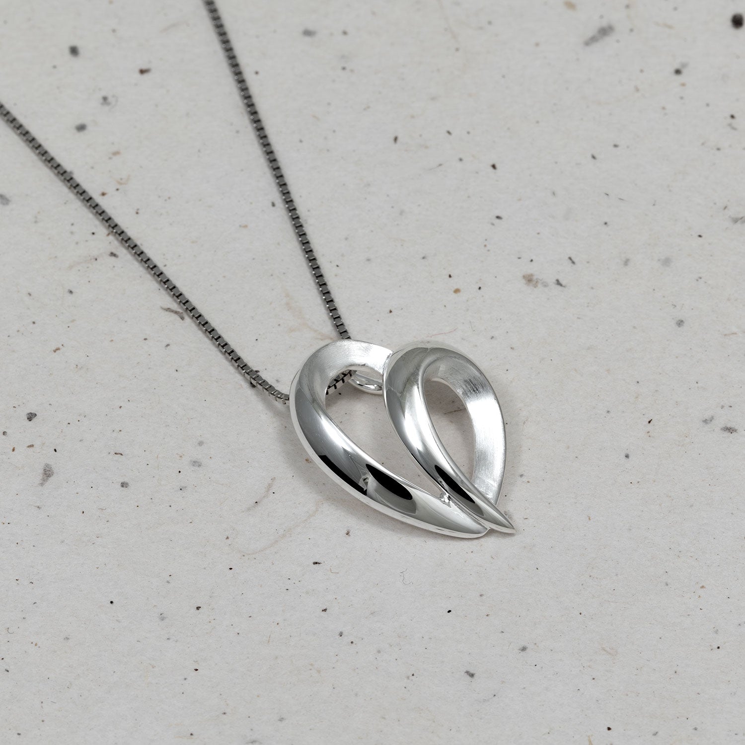 Sleek sterling silver pendant featuring a flowing, leaping heart-inspired design suspended from a fine chain, embodying modern elegance and sculptural form.