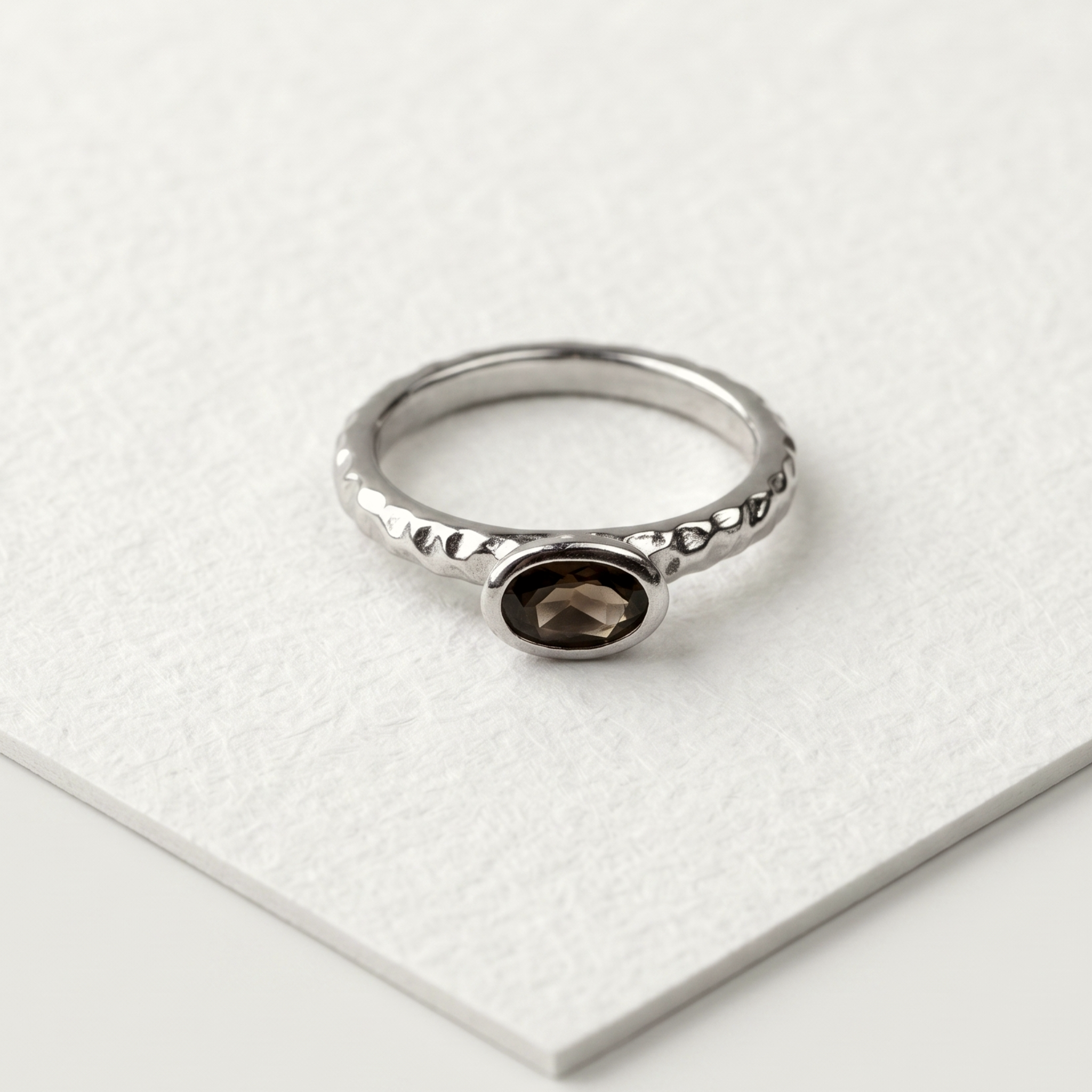 A sterling silver ring with a faceted smoky quartz gemstone set in the center, featuring a textured hammered effect on the band.