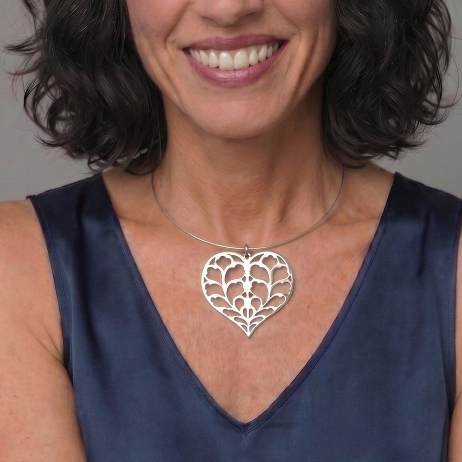 Sterling silver pendant in a sculptural heart design featuring cut-out leaf motifs, suspended on a smooth omega collar necklace, styled with a deep blue silk top.