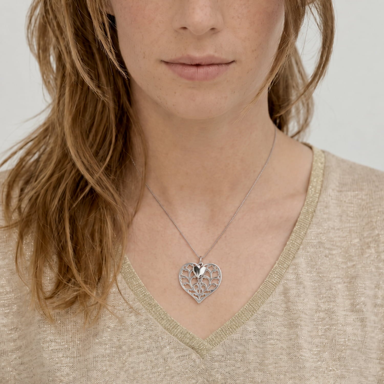Sterling silver necklace featuring a detailed double heart pendant with an openwork design, worn with a classic white button-up shirt for a refined look.
