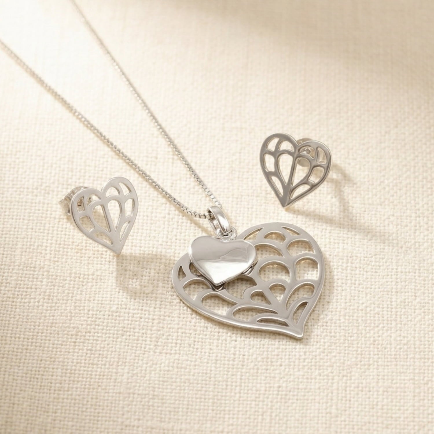 Sterling silver pendant and matching stud earrings featuring a sculptural double heart design with openwork detailing, presented on a fine snake chain.