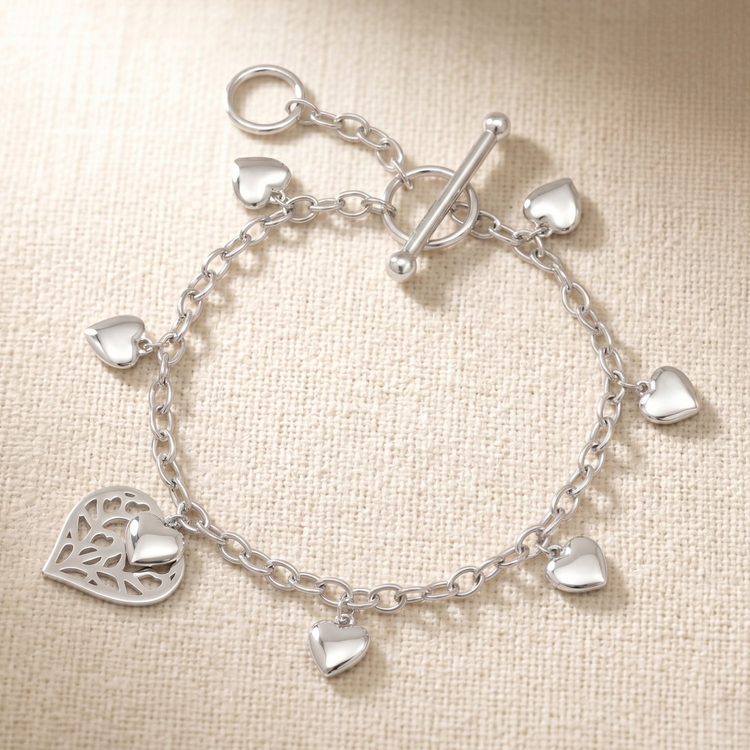 Sterling silver chain bracelet featuring a sculptural heart pendant and smaller heart charms, secured with a T-bar clasp, showcasing elegant British silver jewellery design.