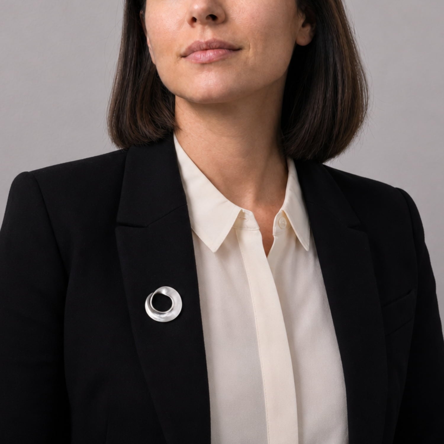 Model wears twisting sterling silver circle brooch on black blazer