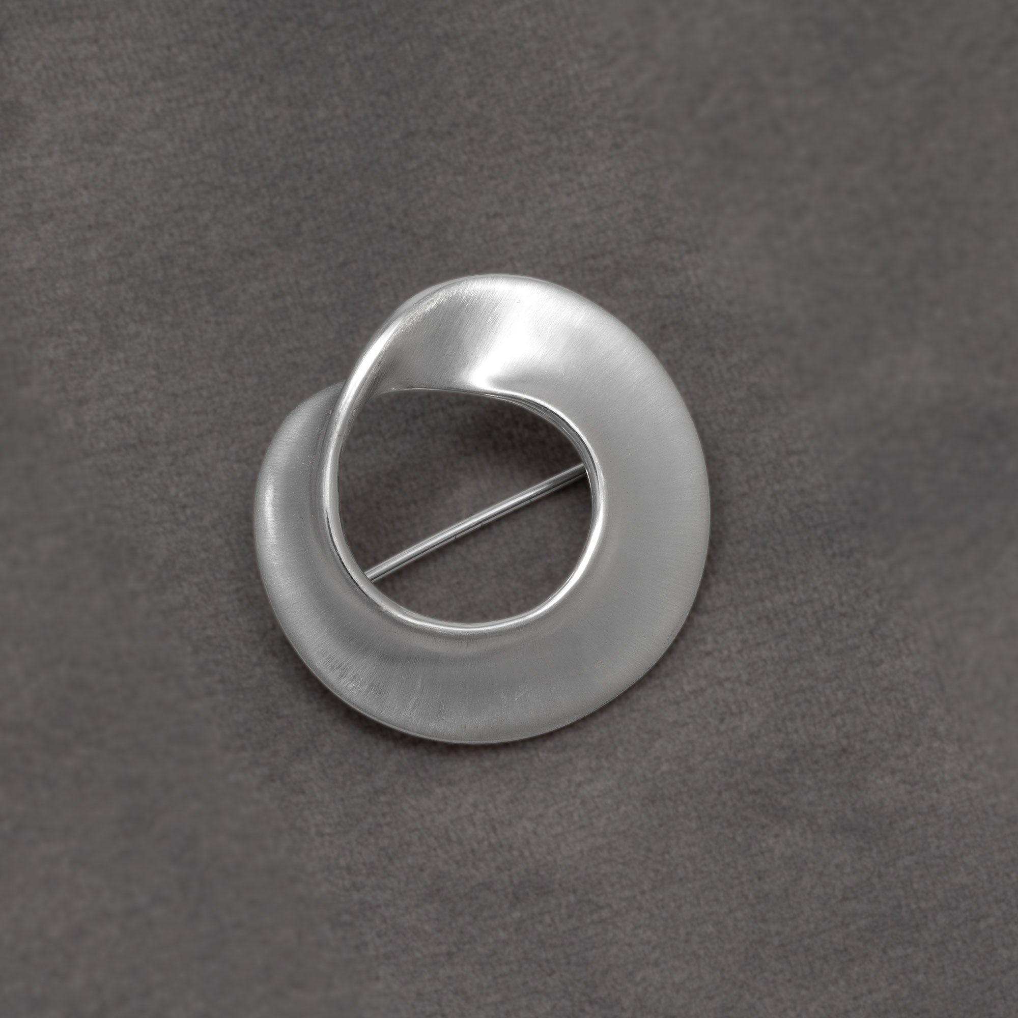 Twisting sterling silver circle brooch on a grey background