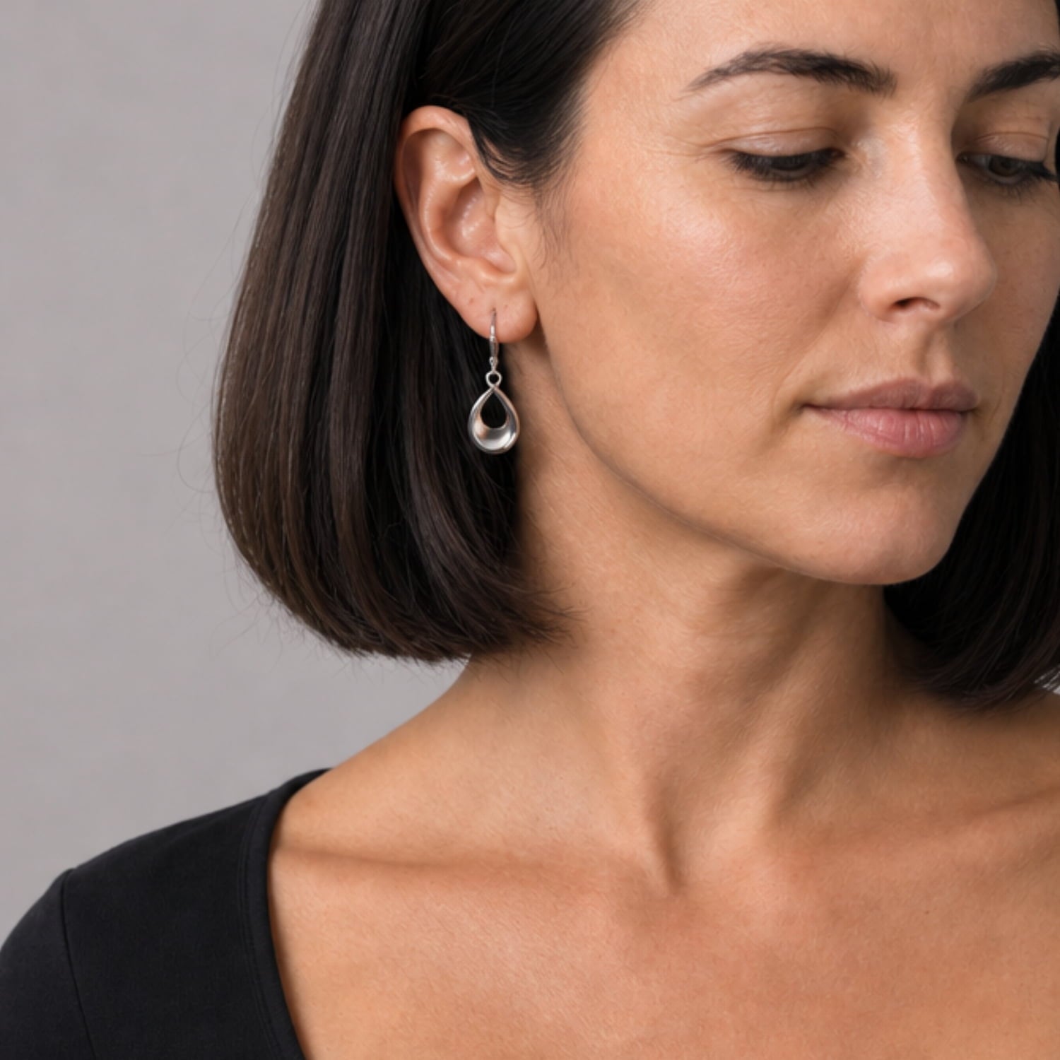 Model wears a pair of polished sterling silver earrings featuring open teardrop shapes with smooth, sculptural contours and secure lever-back clasps for elegant everyday wear.