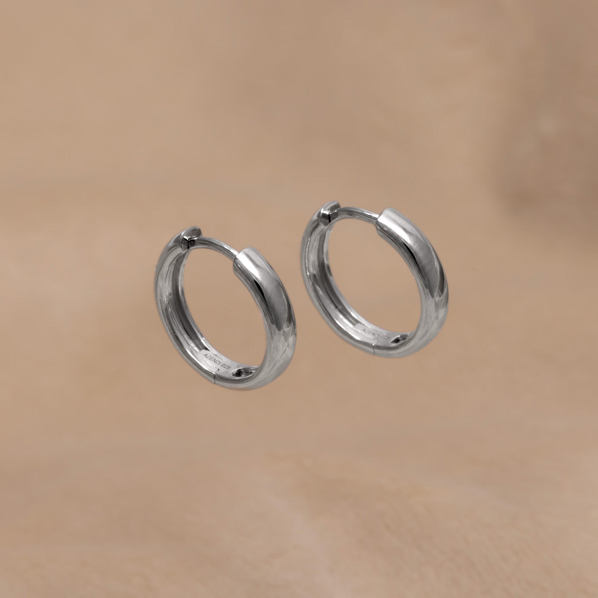Small rounded sterling silver hoop earrings with a polished finish and hinged closure, offering a minimalist and timeless design in fine silver jewellery.  Placed on a cream velvet cloth.