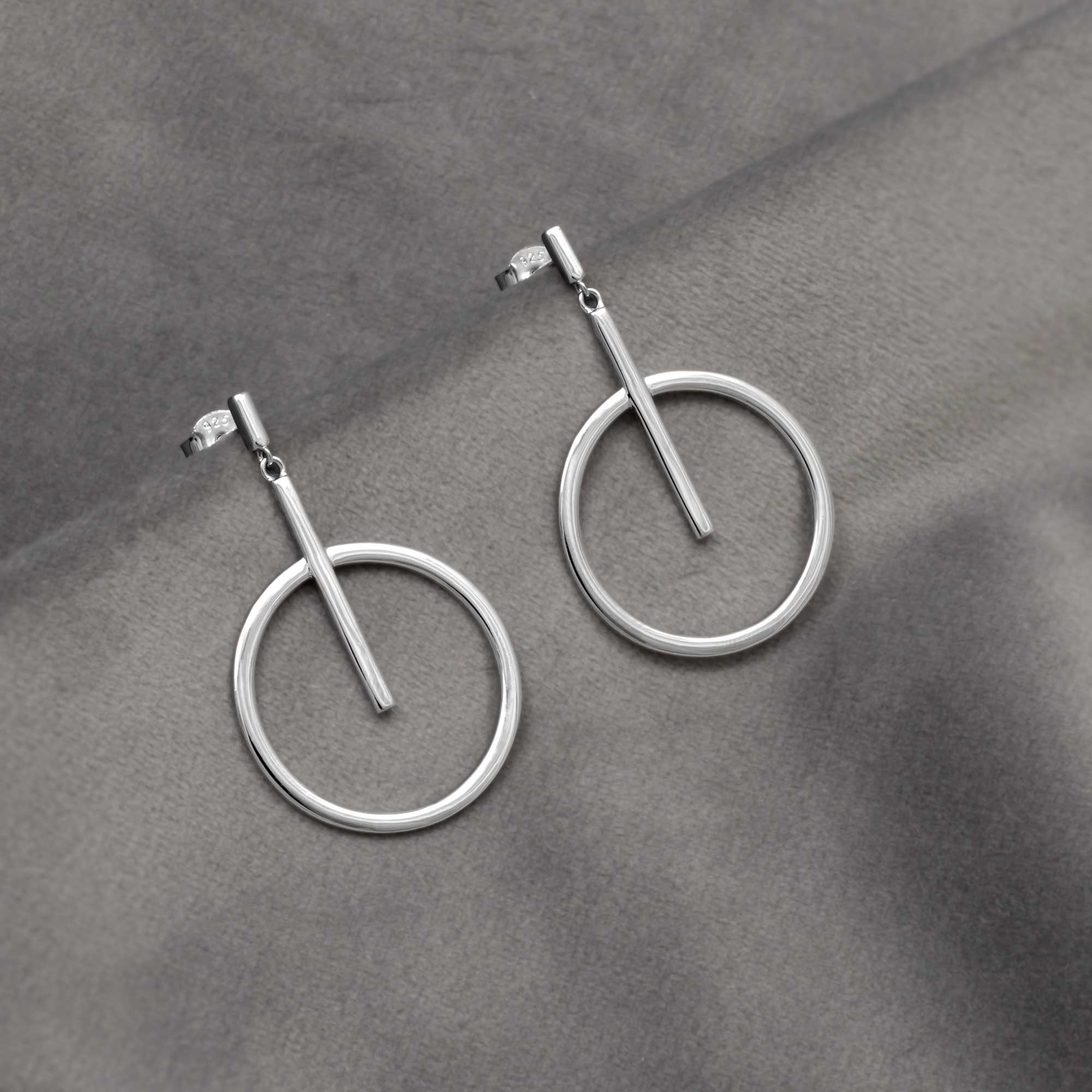 Silver circle and line drop earrings on a gray surface
