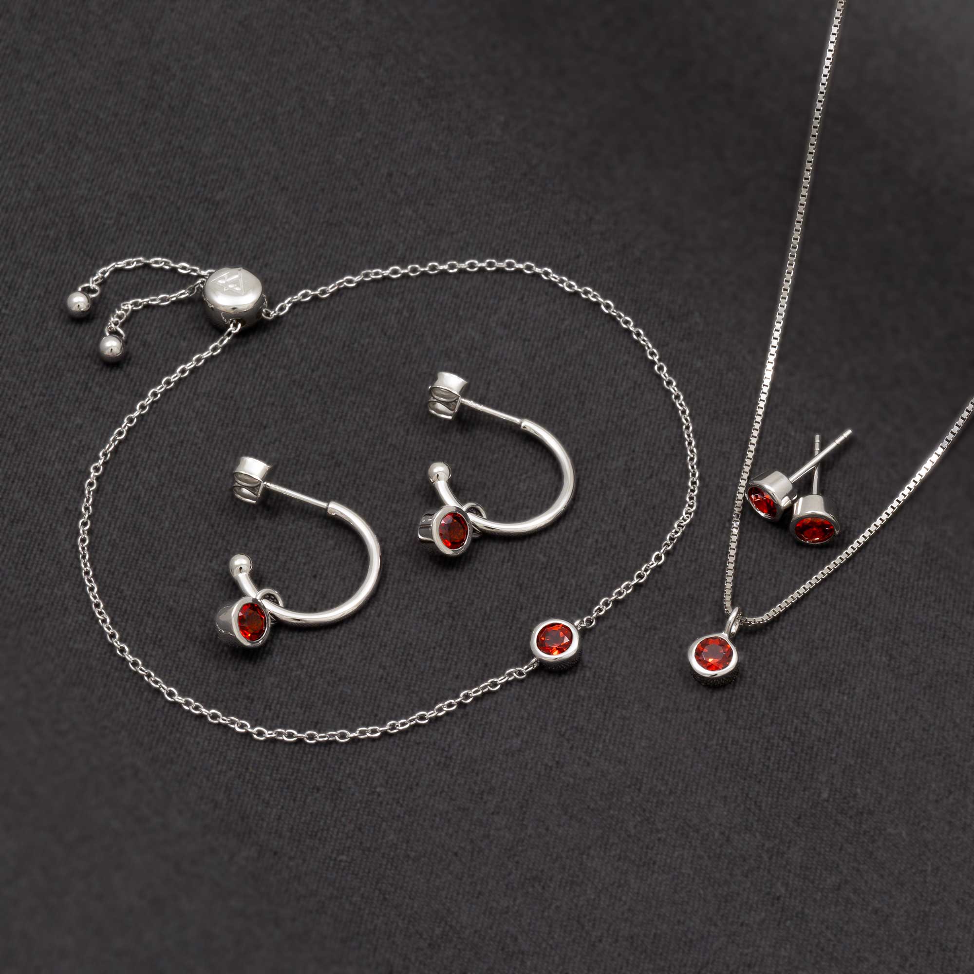 Sterling silver hoop earrings and matching stud earrings with deep red garnet stones, styled alongside a delicate silver chain bracelet and pendant for a cohesive, elegant look.