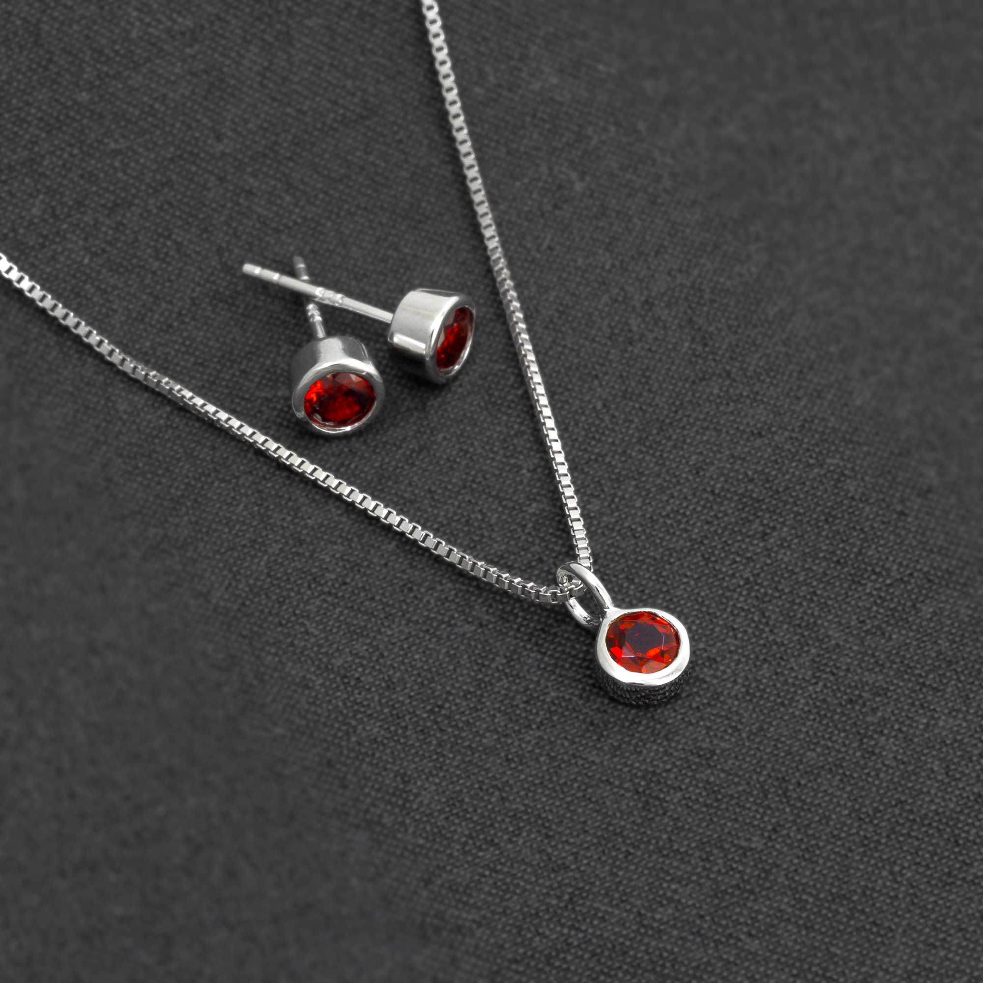 Sterling silver necklace and stud earrings featuring deep red garnet gemstones, showcasing a minimalist and sculptural design on a dark textured background.