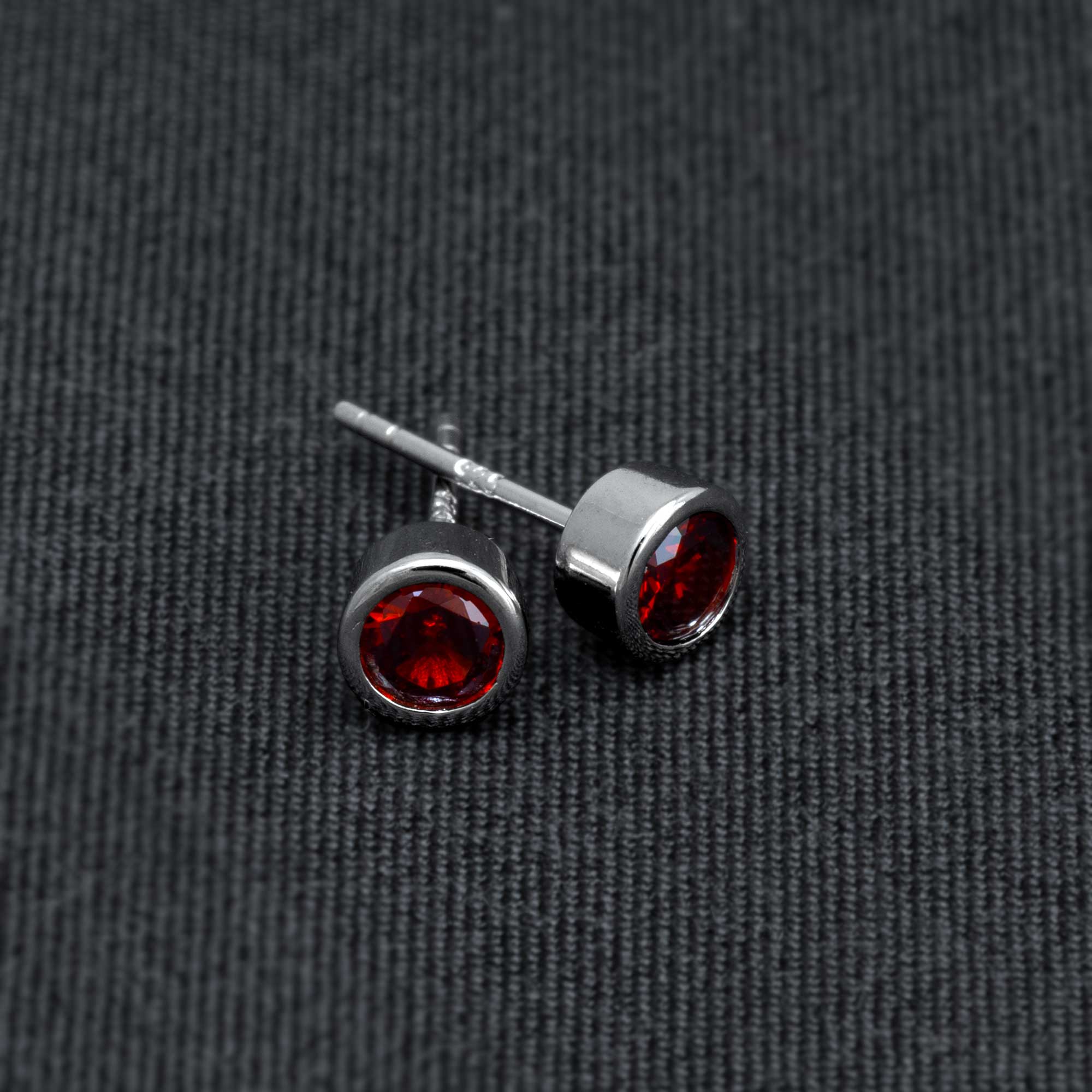 Pair of sterling silver stud earrings featuring deep red garnet gemstones set in a sleek, polished bezel design, reflecting expert British craftsmanship.
