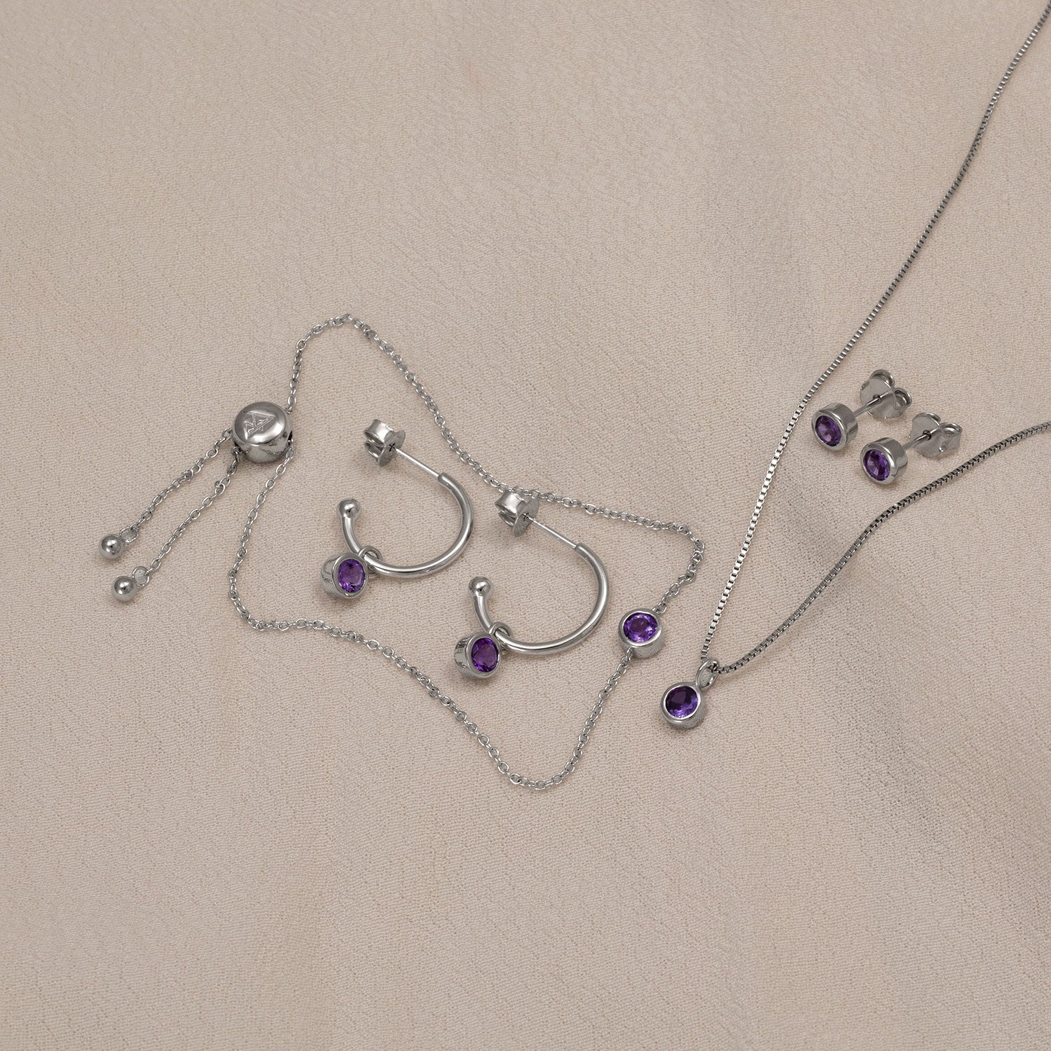 Sterling silver hoop earrings, necklace, stud earrings, and adjustable bracelet set featuring faceted amethyst stones, showcasing contemporary sculptural jewellery design.
