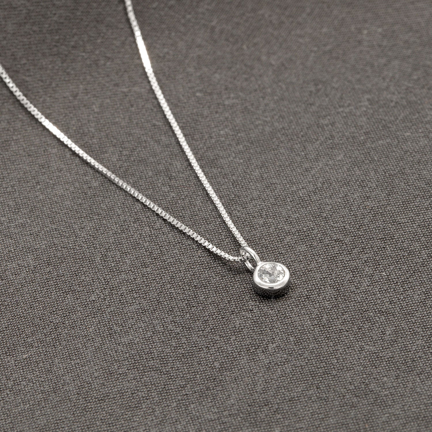 Delicate sterling silver pendant featuring a round white topaz gemstone, suspended on a fine chain and displayed on a soft grey fabric, embodying elegant British craftsmanship.