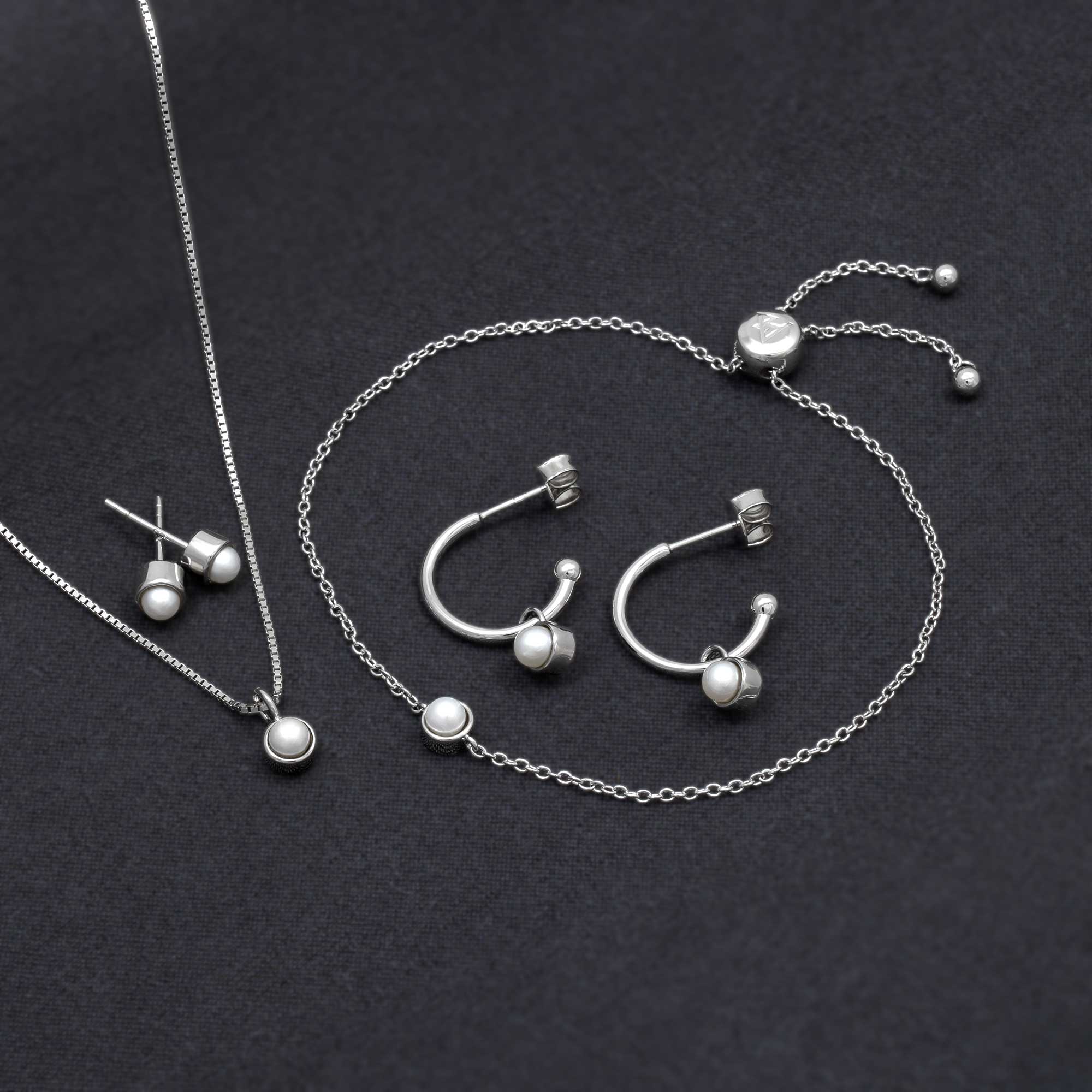 A delicate sterling silver jewellery set featuring hoop earrings, a pendant necklace, and an adjustable bracelet, each adorned with lustrous freshwater pearls on fine chains.