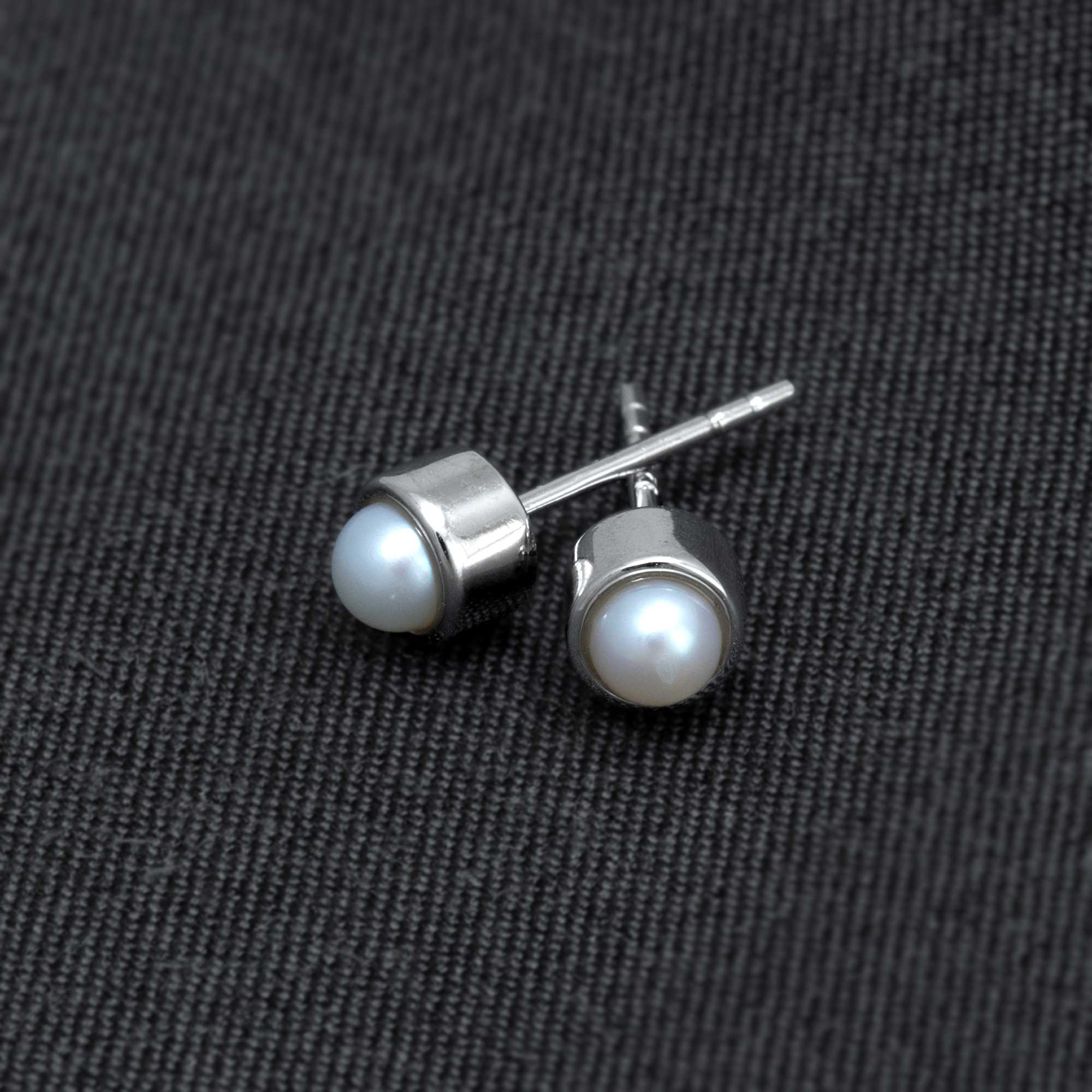 Pair of sterling silver stud earrings featuring lustrous freshwater pearls set in a sleek, modern bezel design, reflecting expert British craftsmanship.