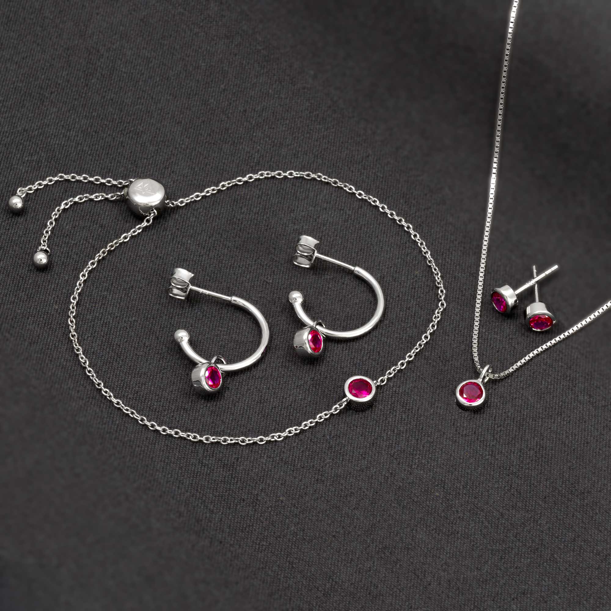 Delicate sterling silver jewellery set featuring ruby gemstones, including hoop earrings, stud earrings, and a pendant on fine chains, highlighting expert British craftsmanship.