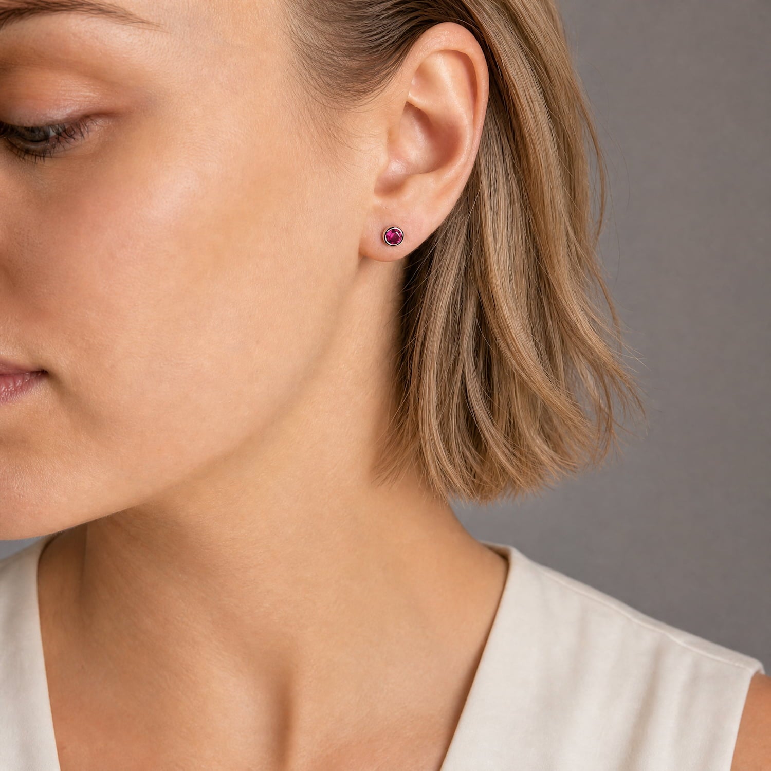 Model wears a pair of sterling silver stud earrings featuring deep red ruby gemstones set in smooth bezels, showcasing minimalist yet elegant craftsmanship by a British jeweller.