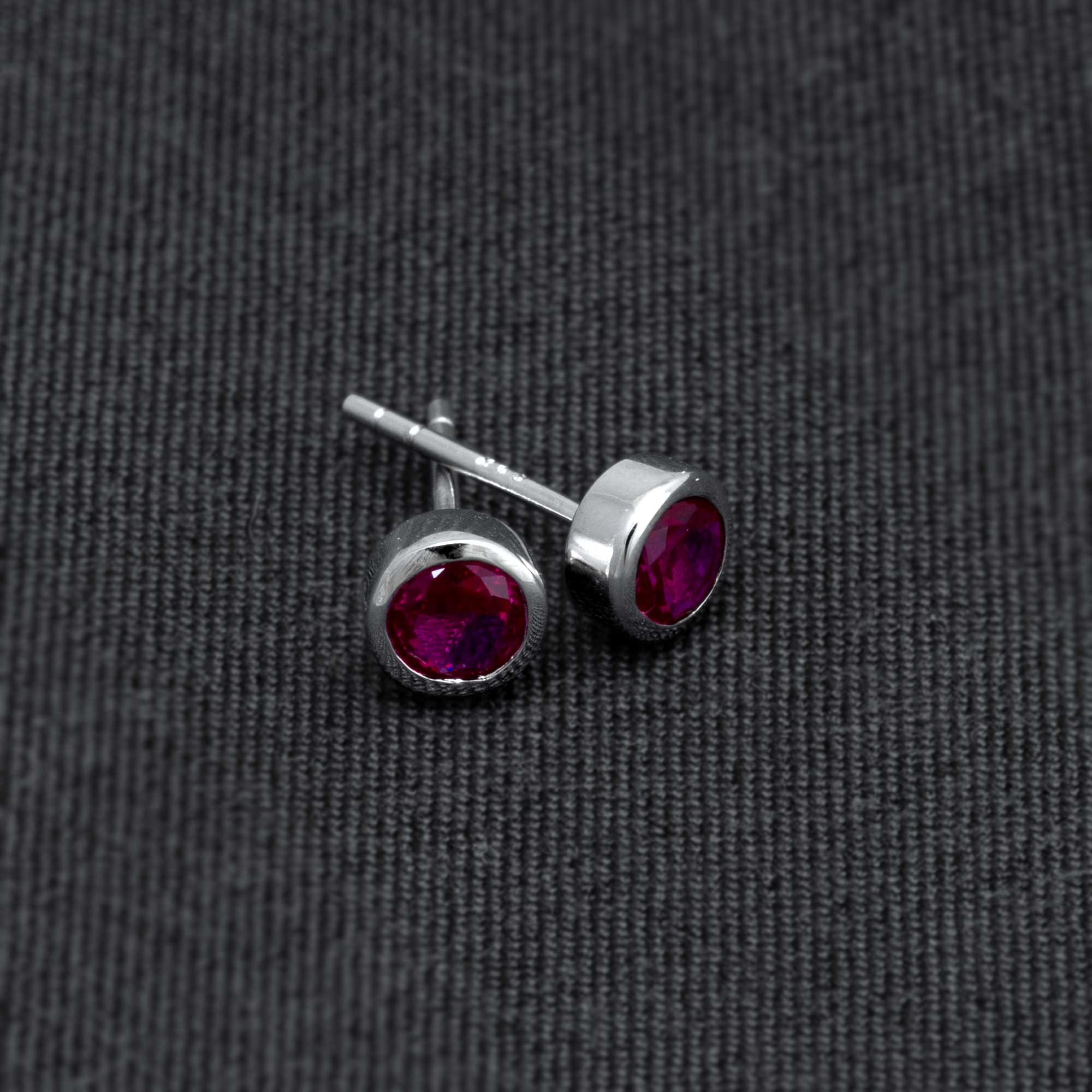 Pair of sterling silver stud earrings showcasing deep red ruby gemstones in a sleek, modern bezel setting, embodying refined British craftsmanship.