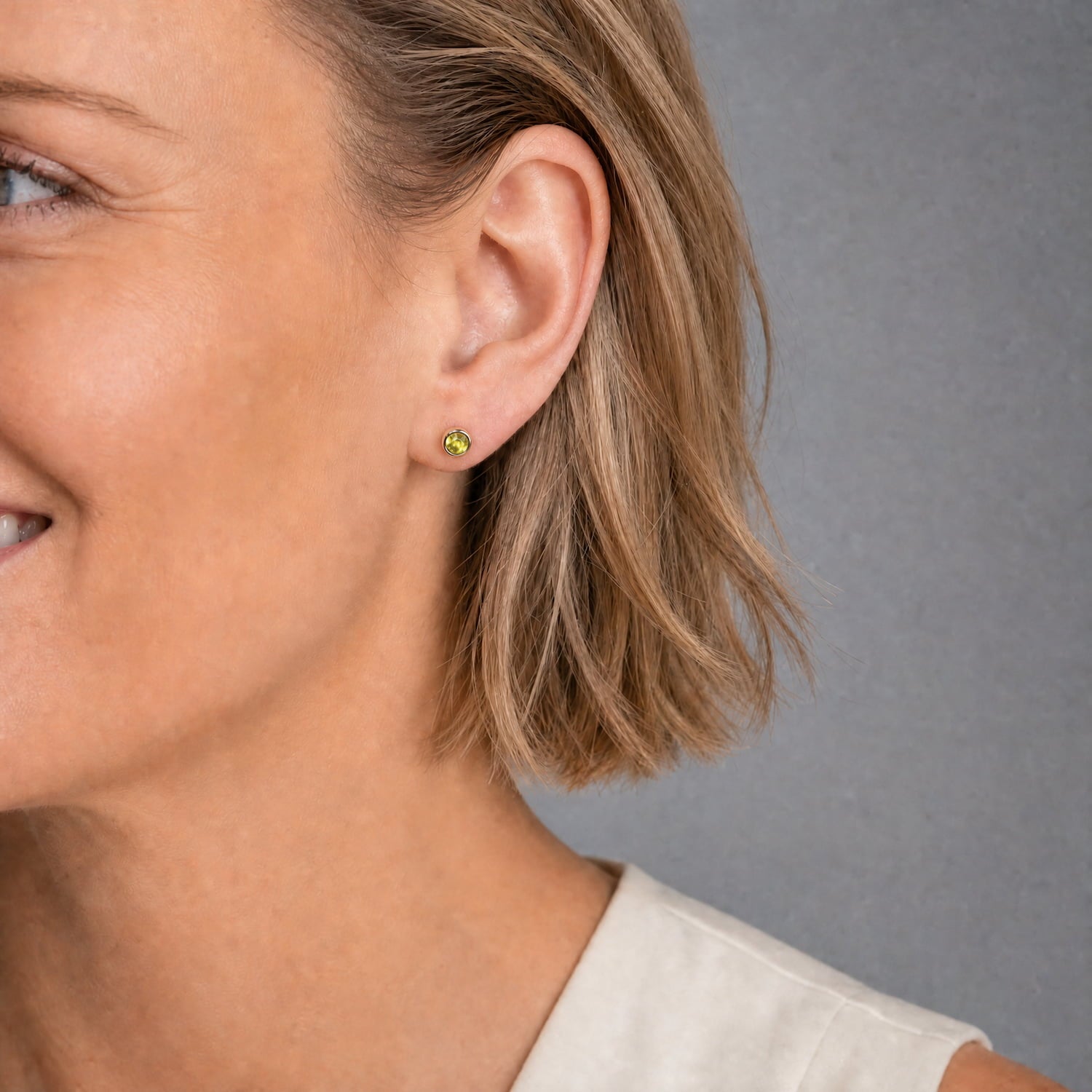 Model wears contemporary sterling silver stud earrings featuring vibrant peridot gemstones, showcasing a clean, minimalist design crafted with expert British precision.