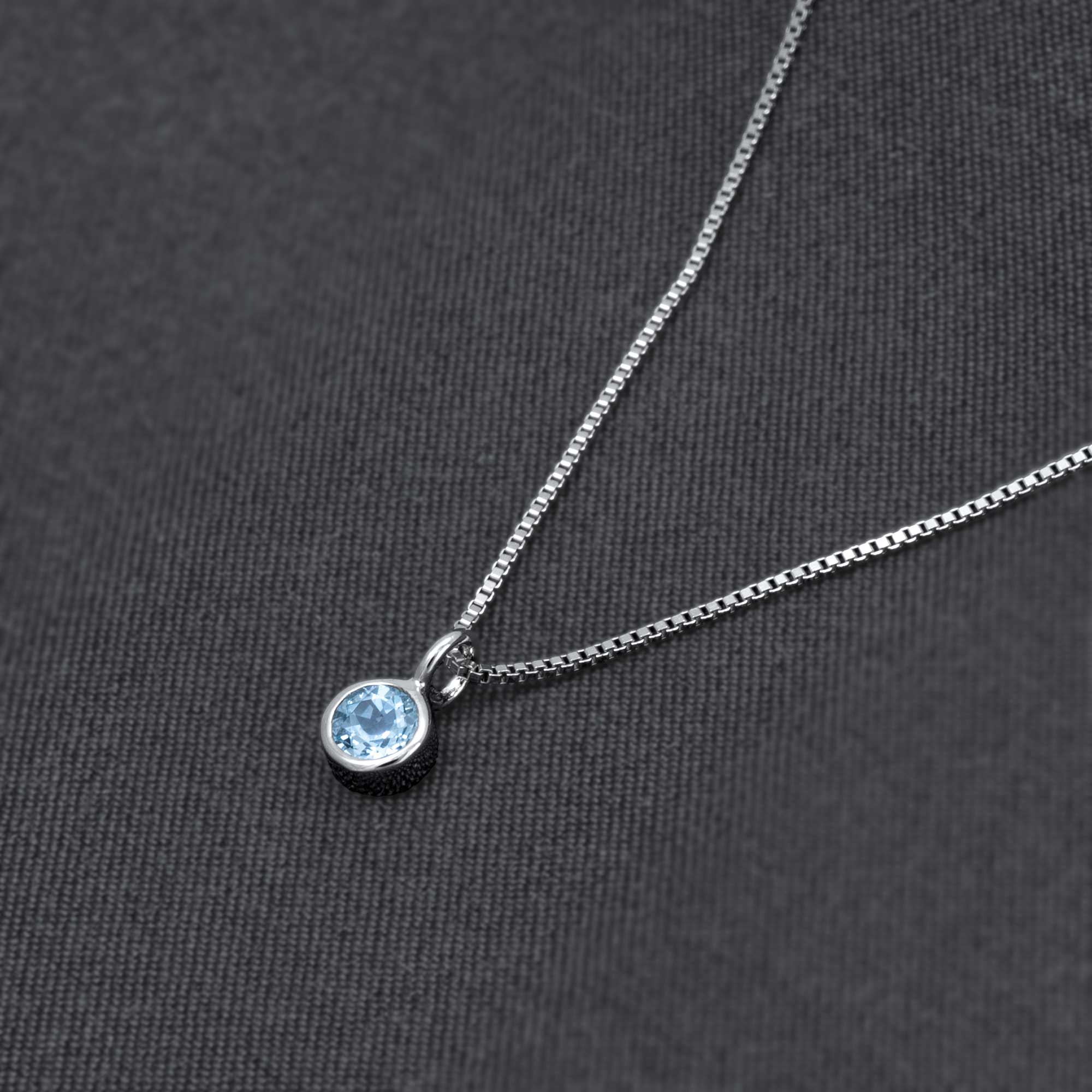 Delicate sterling silver pendant featuring a bezel-set blue topaz gemstone on a fine chain, showcasing expert British craftsmanship and contemporary design.