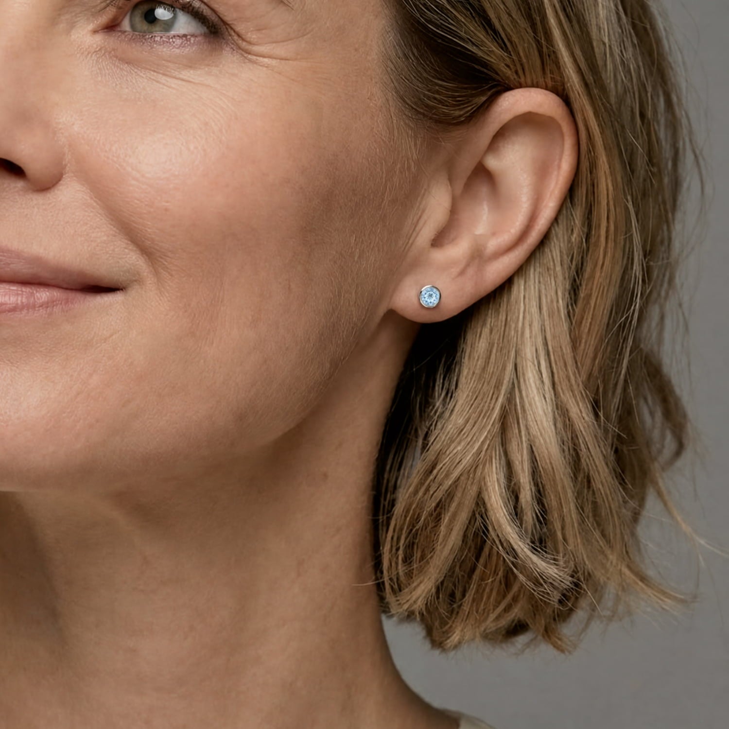 Pair of sterling silver stud earrings featuring round blue topaz gemstones set in a polished bezel setting, showcasing a refined and contemporary design.