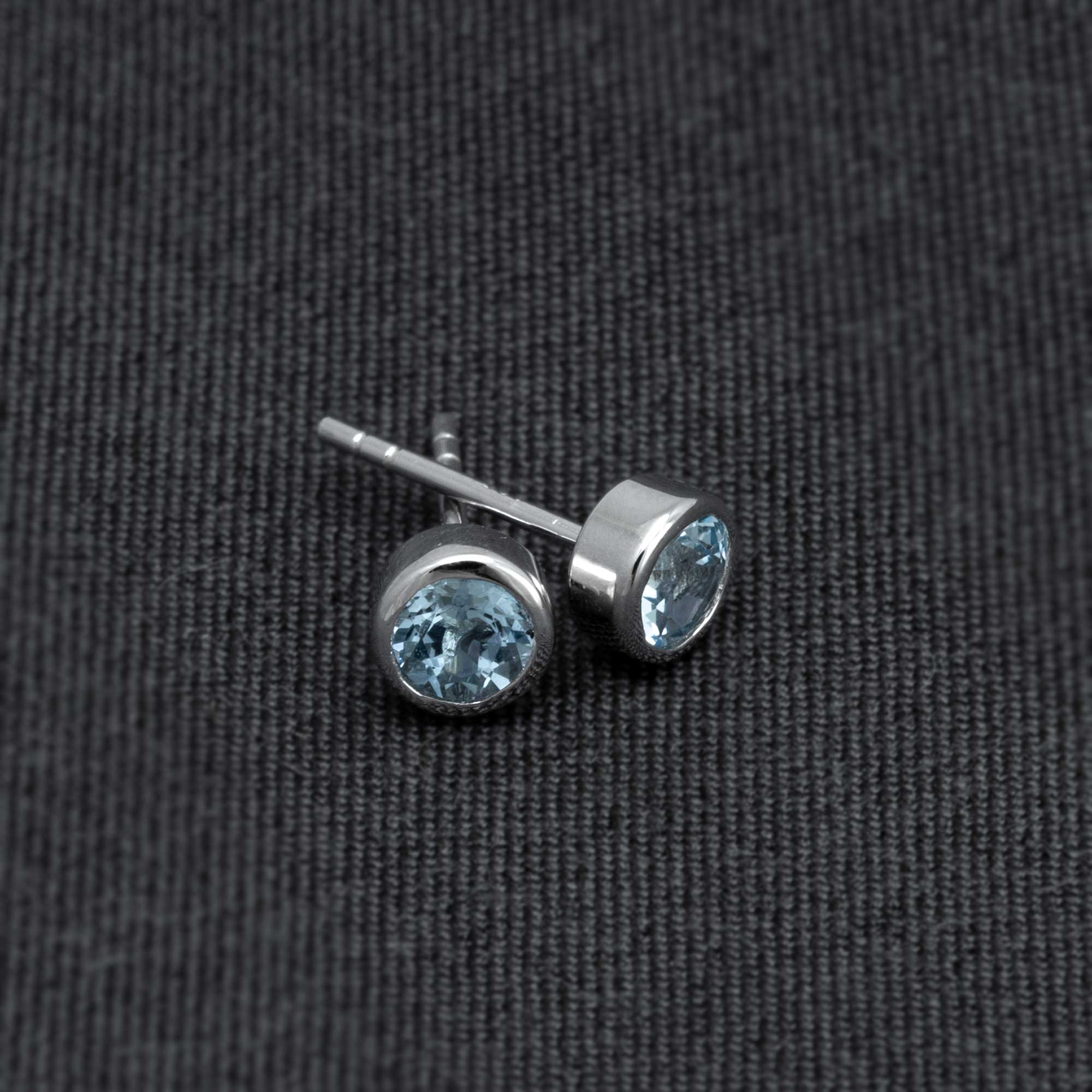 Pair of sterling silver stud earrings featuring round blue topaz gemstones set in a polished bezel setting, showcasing a refined and contemporary design.