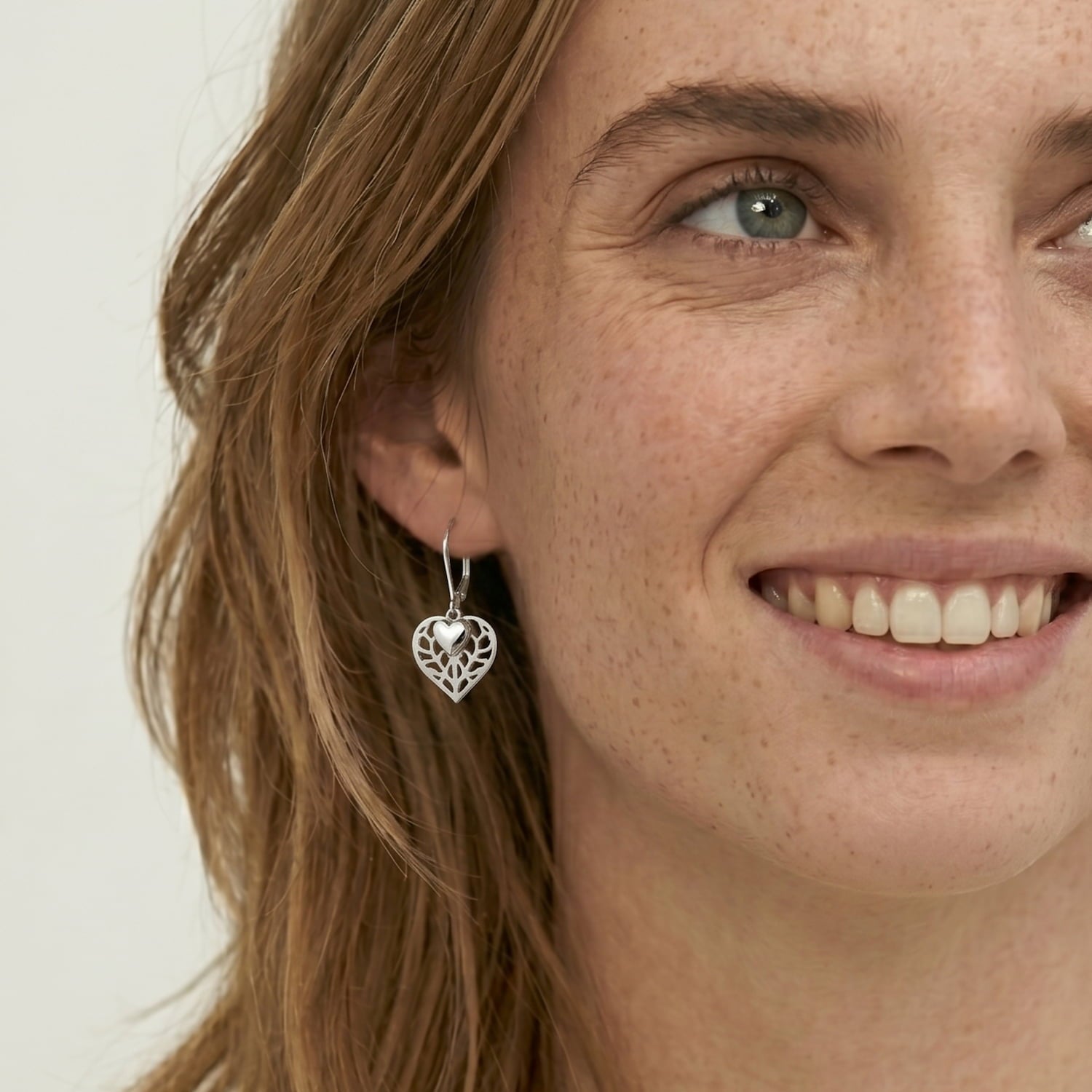 Model wears sterling silver double heart drop earring featuring an openwork heart design with a smaller polished heart charm, handcrafted for a contemporary and elegant look.