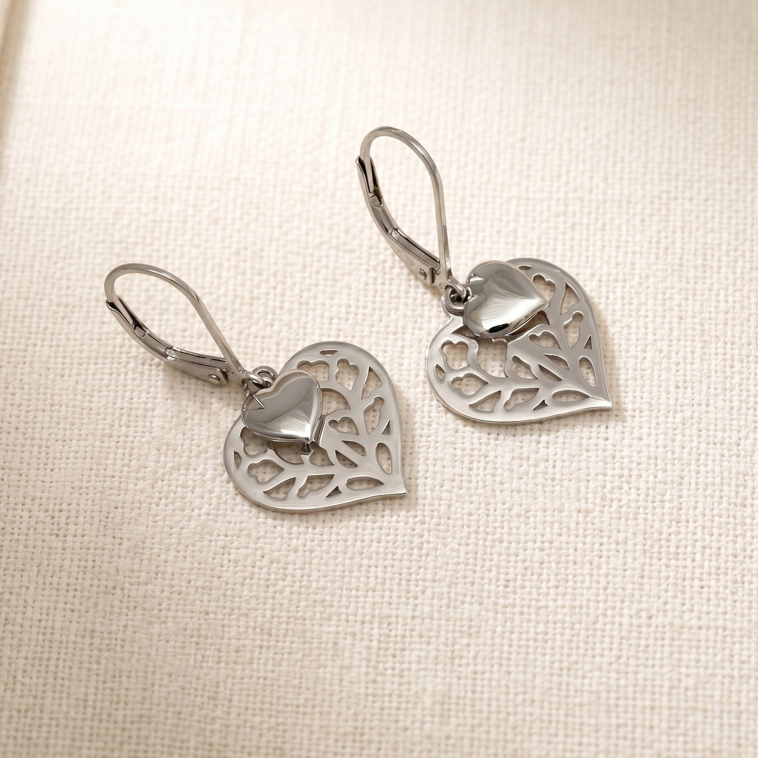 Pair of sterling silver double drop earrings featuring sculptural openwork hearts with a smooth polished heart overlay, designed with lever-back clasps for secure wear.