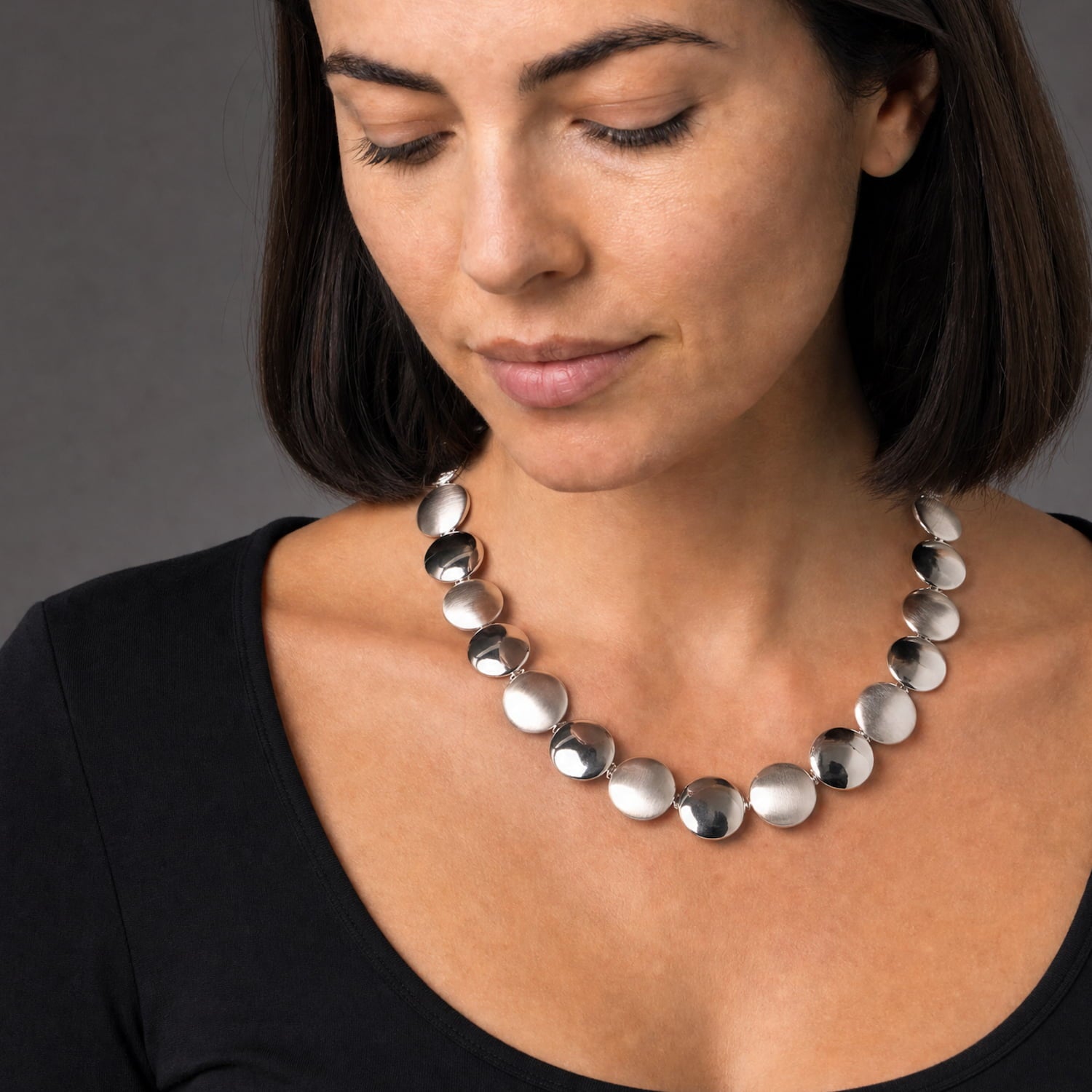 Woman wears a sterling silver necklace featuring alternating satin and polished round buttons linked together, offering adjustable length with a sleek, modern design by Azendi.
